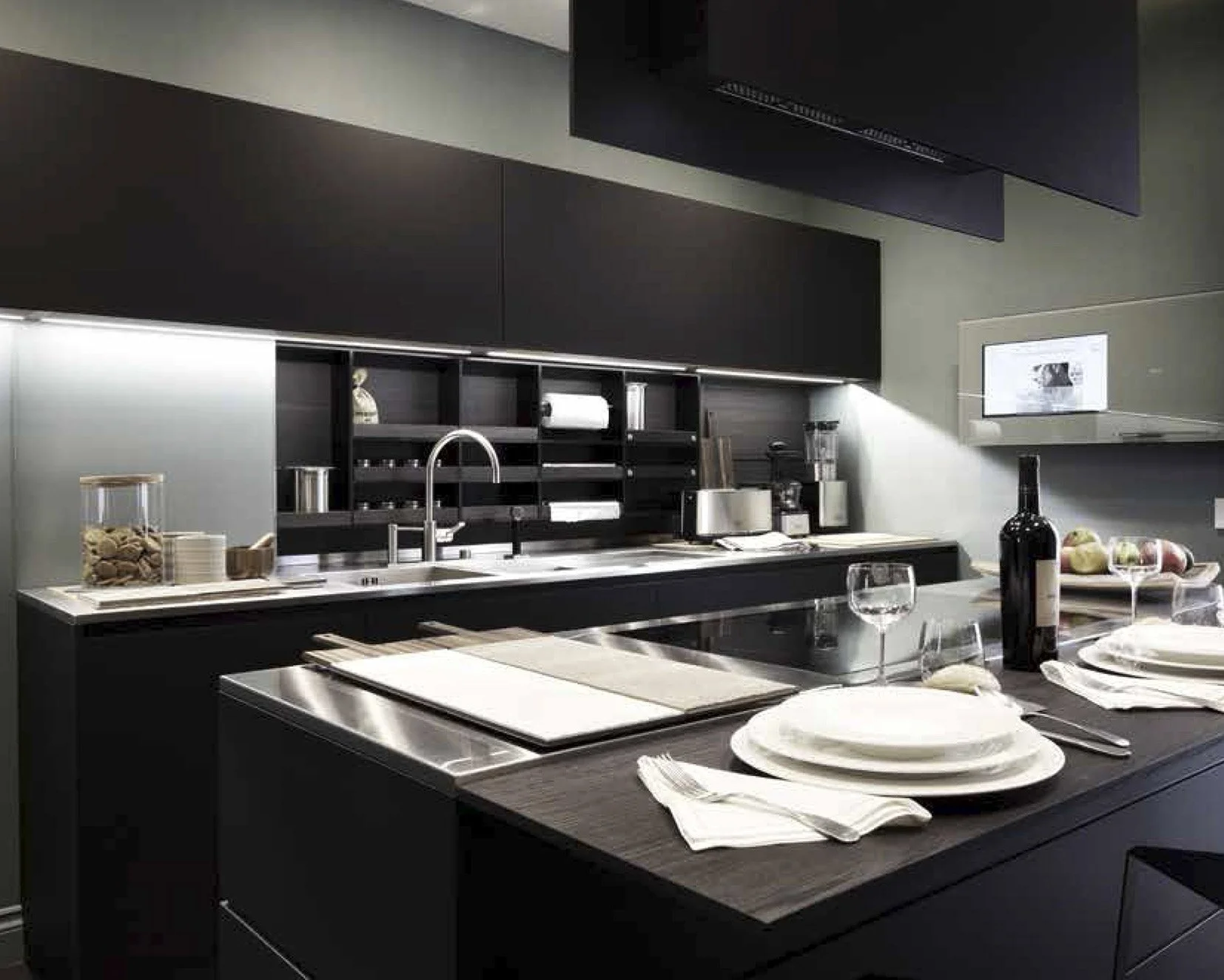 Cucina moderna nera con tavolo apparecchiato, bicchieri di vino, piatti e posate, bottiglia di vino e ingredienti.