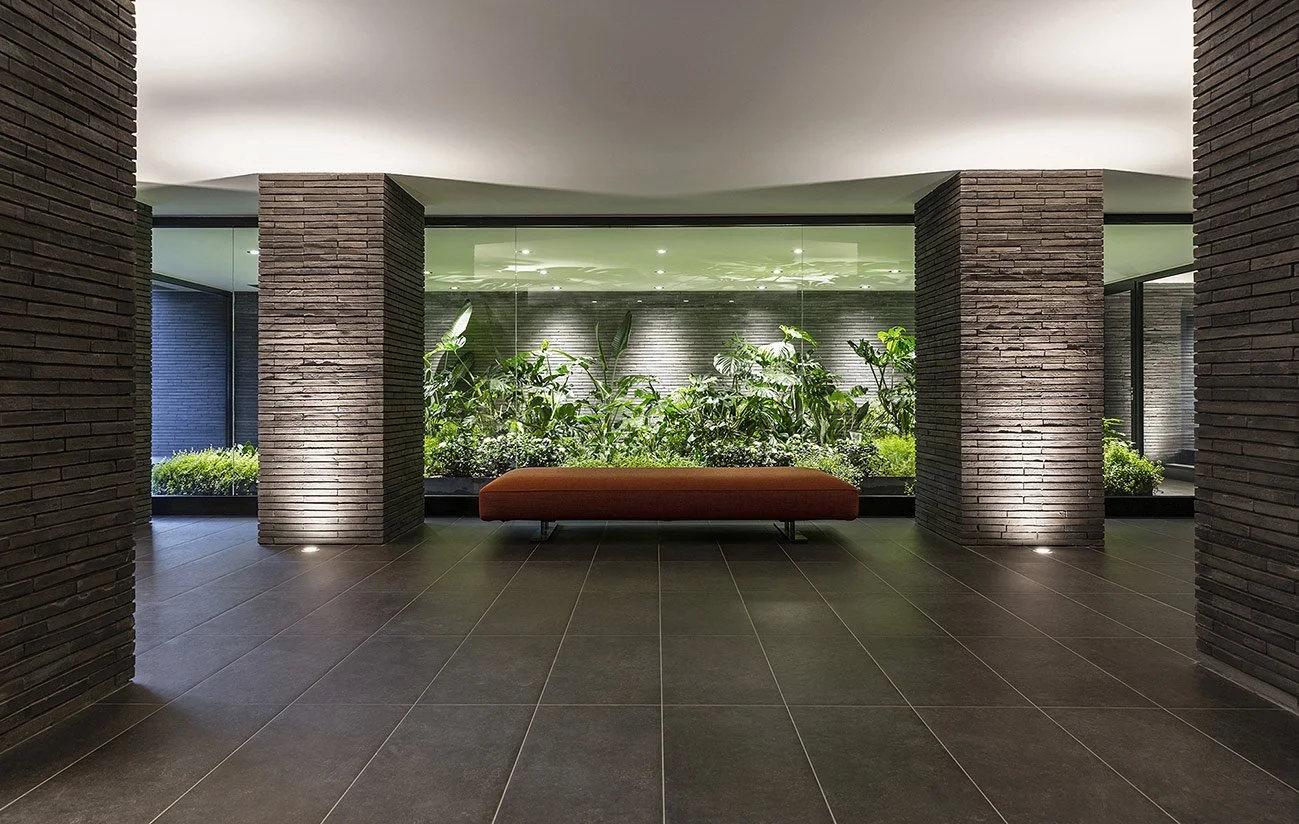 Ingresso di un edificio moderno con piante e una panchina marrone.