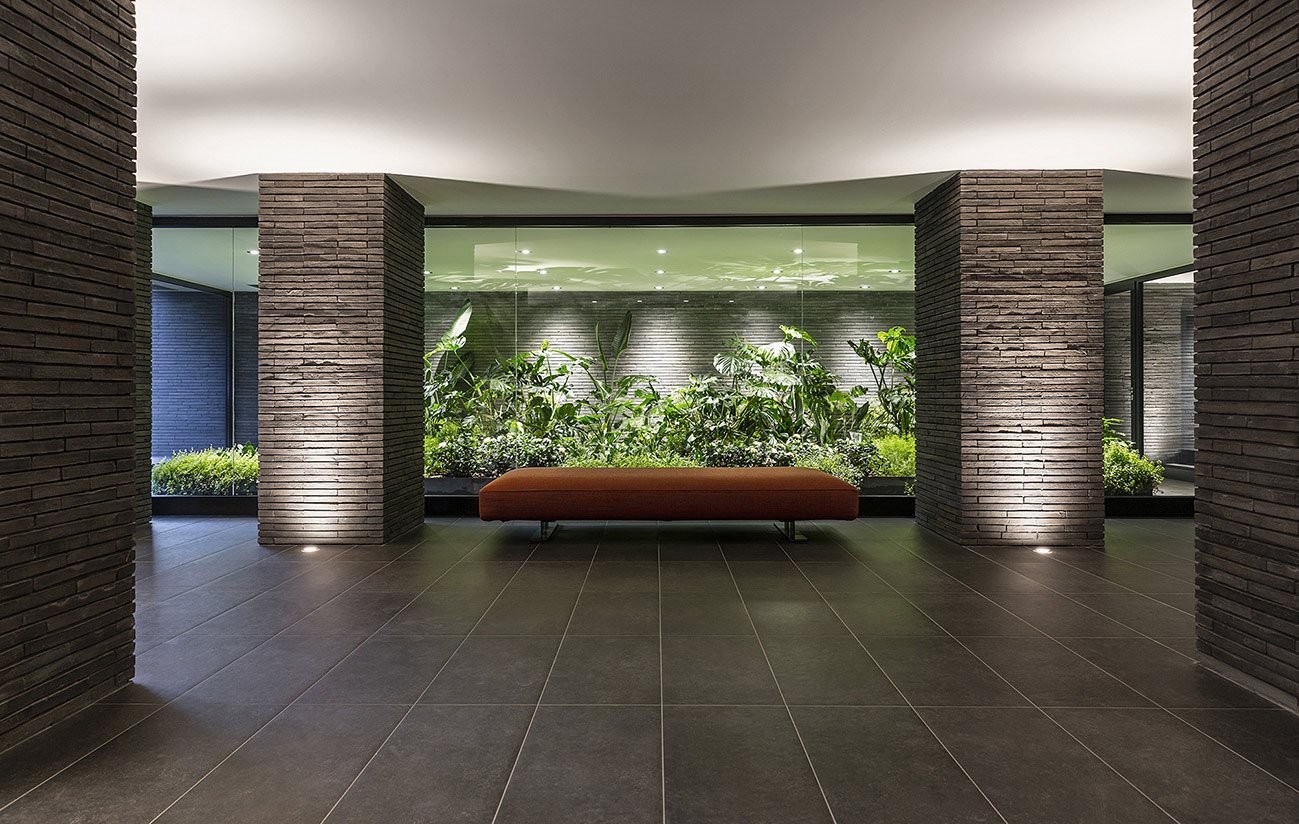 Interno di un edificio moderno con pareti in mattoni scuri e grande finestra con piante verdi davanti.