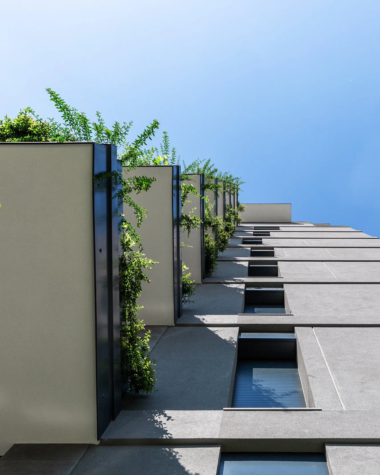 Immagine di un edificio moderno con balconi e piante verdi lungo la facciata, vista dall'angolazione con il cielo azzurro sullo sfondo.
