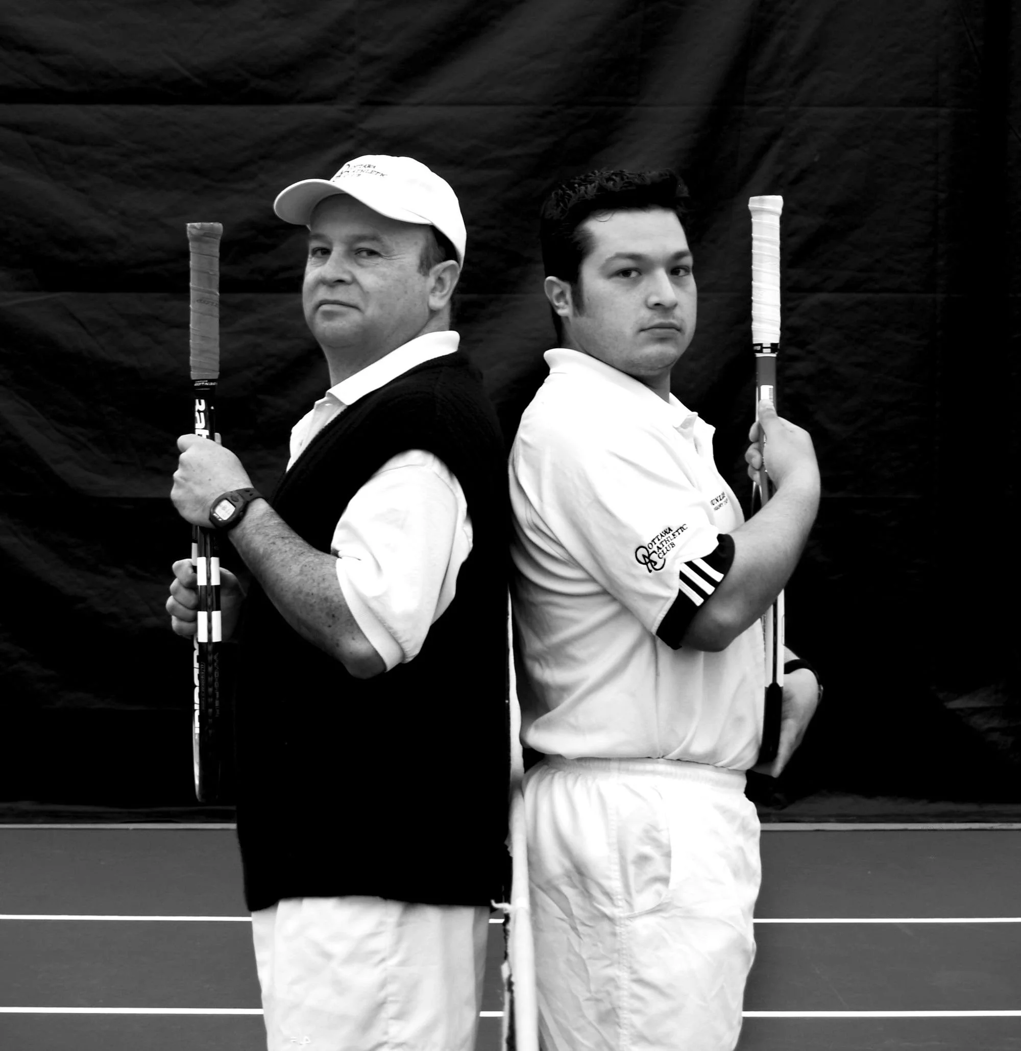 Two male tennis players standing back-to-back holding tennis rackets, with a dark backdrop and lines indicating a tennis court.