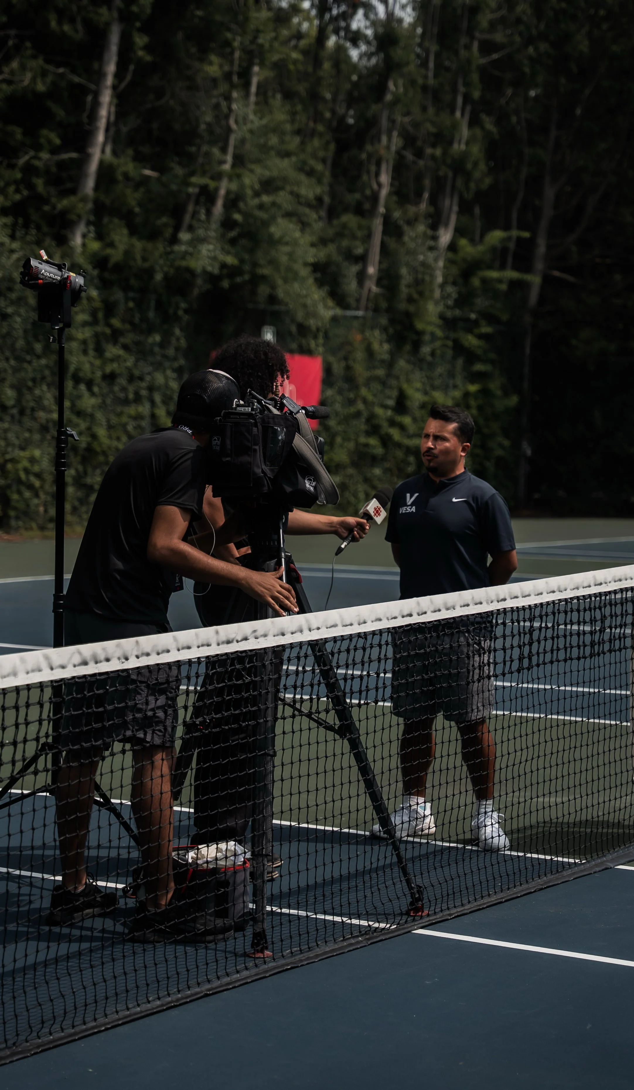 A man being interviewed on a tennis court with a camera crew filming him.