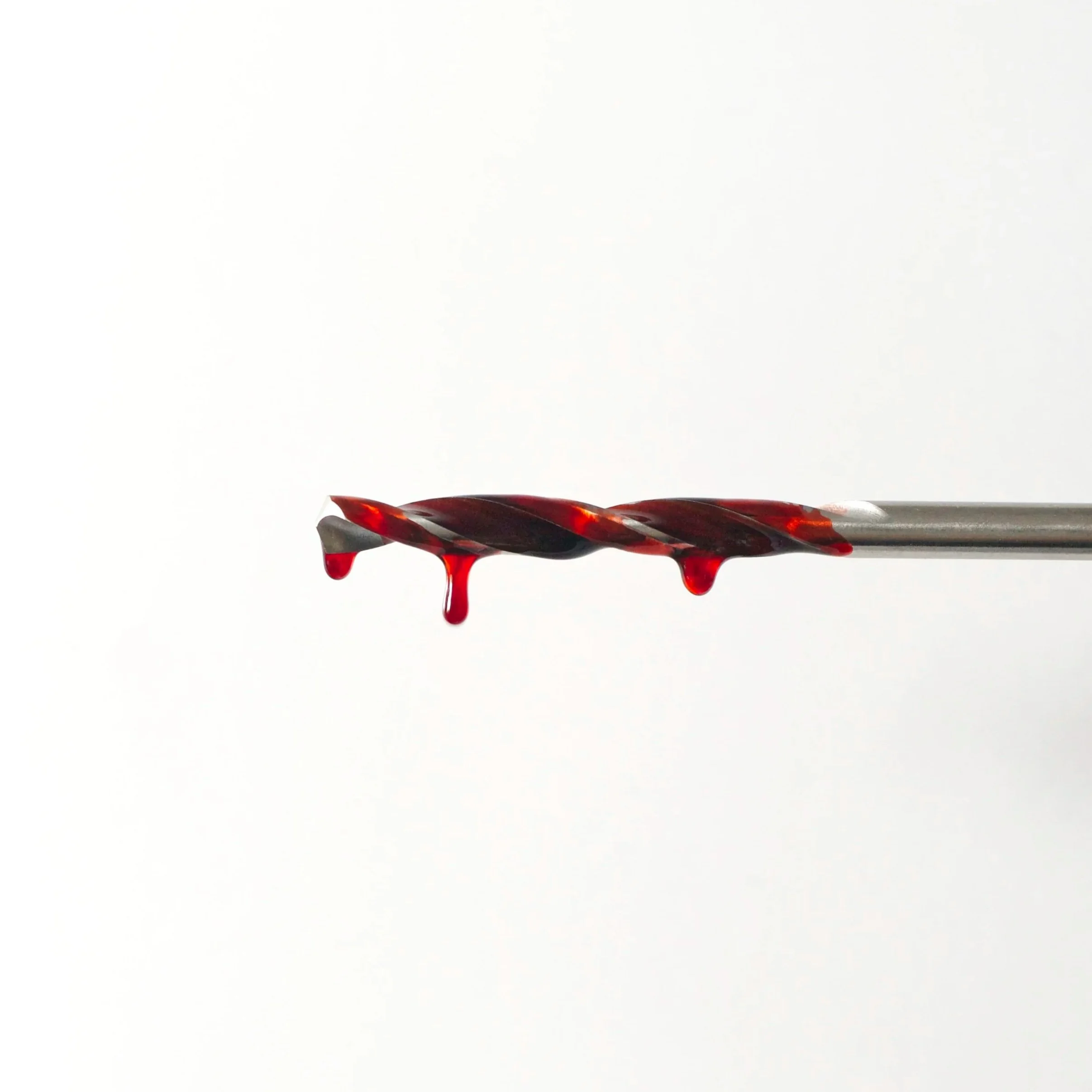 Close-up of a drill bit with red liquid dripping from it against a white background.