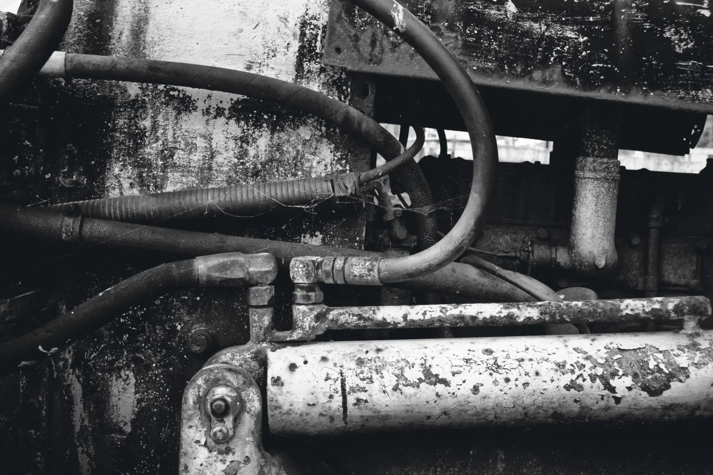 Close-up black-and-white photo of old, rusty vehicle engine parts with water and cobwebs.