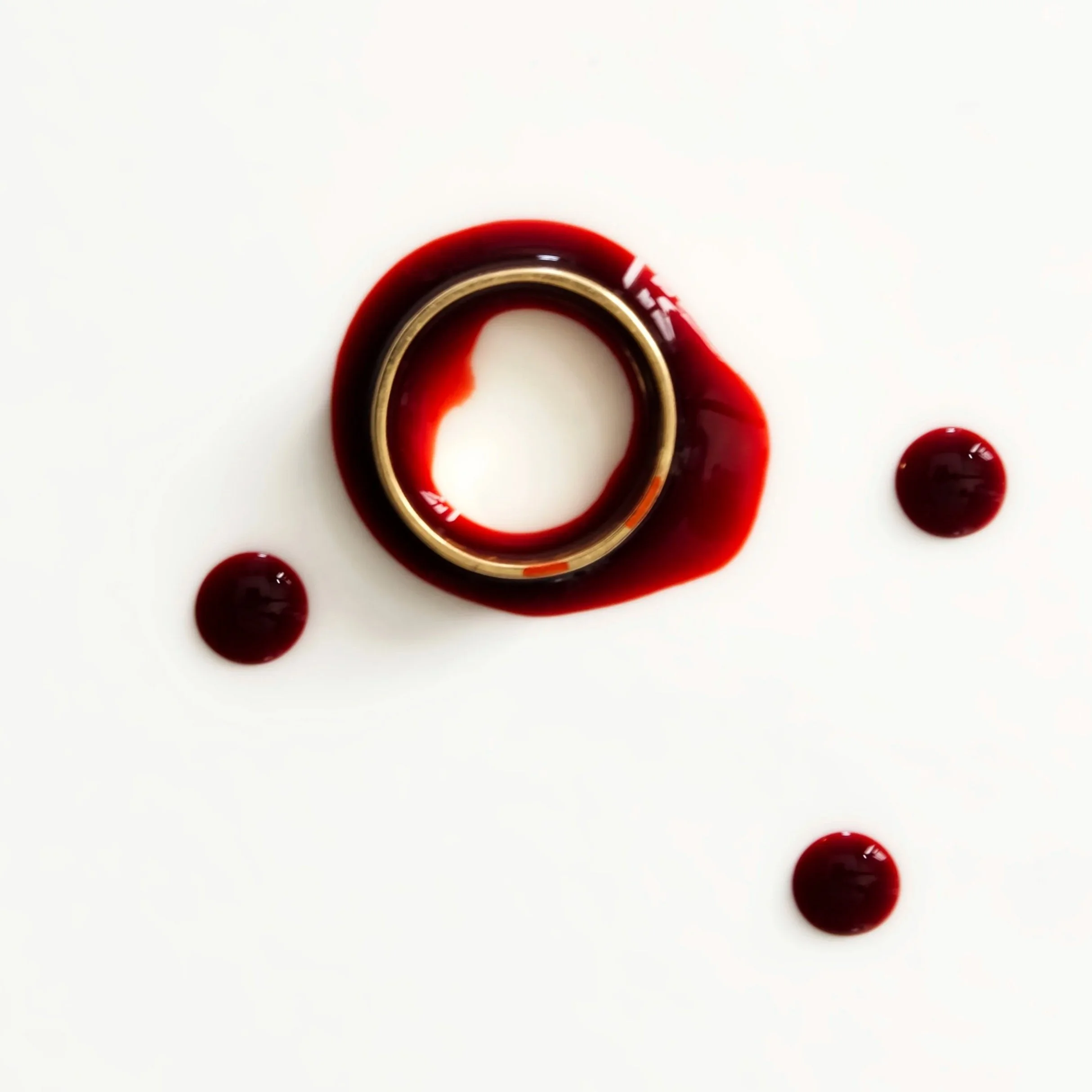 A white surface with a ring and splatters of red liquid, possibly wine or juice, around the ring.