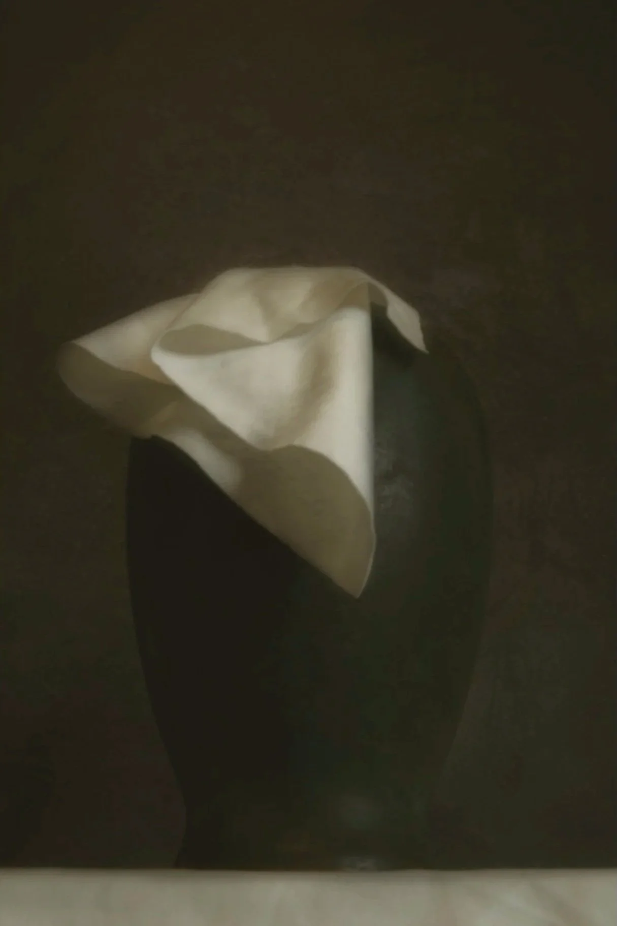 A white tissue or cloth in a black container or vase against a dark background.