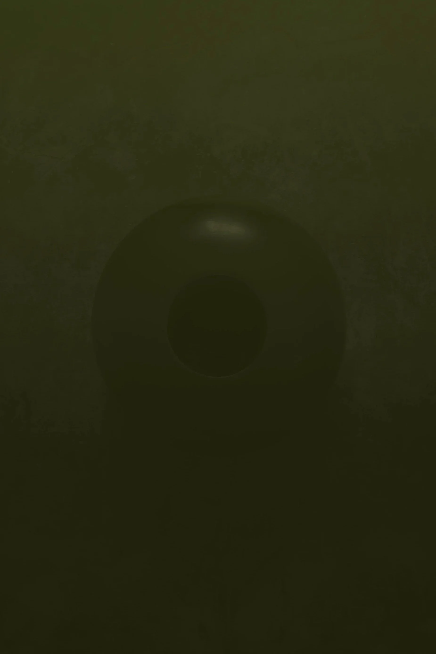 Dark, blurry image of a circular object, possibly a downward-facing camera lens or a similar round object, in a dim or low-light setting.