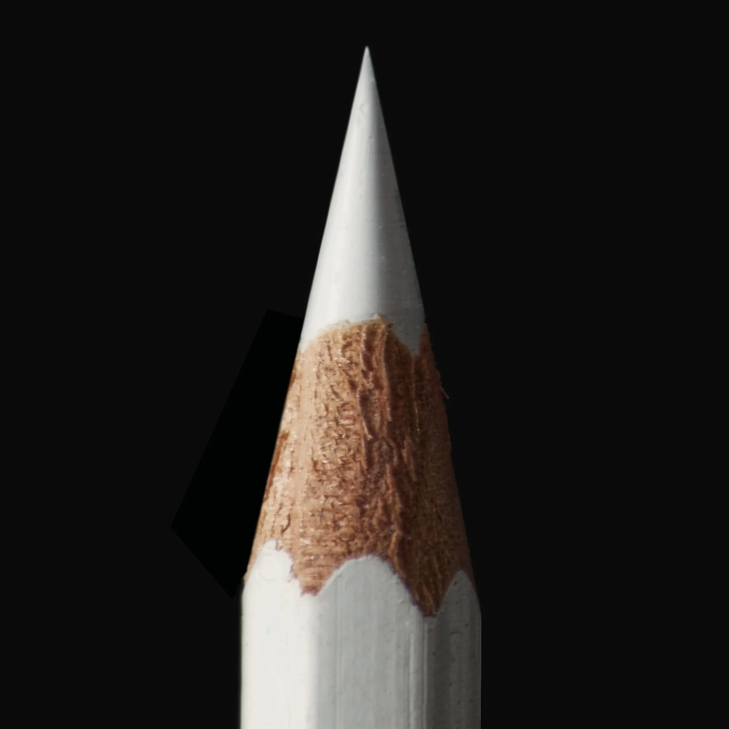 Close-up of a sharpened white colored pencil against a black background.