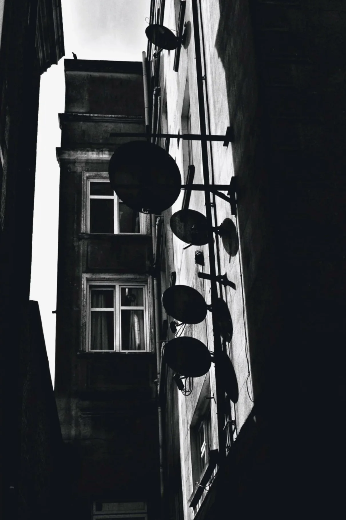 Black and white photo of a rooftop with satellite dishes and equipment, with windows and building walls in the background.