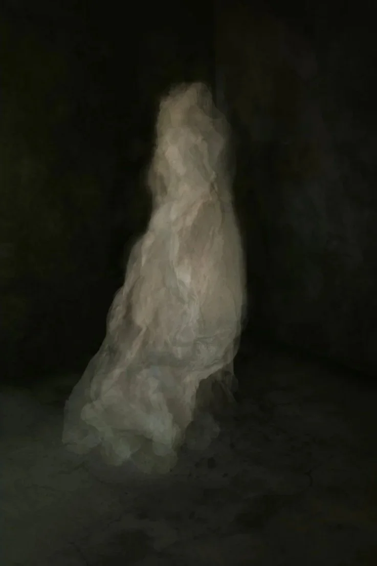 A large, irregularly shaped rock standing on a cracked, dark floor in a dark room or cave.