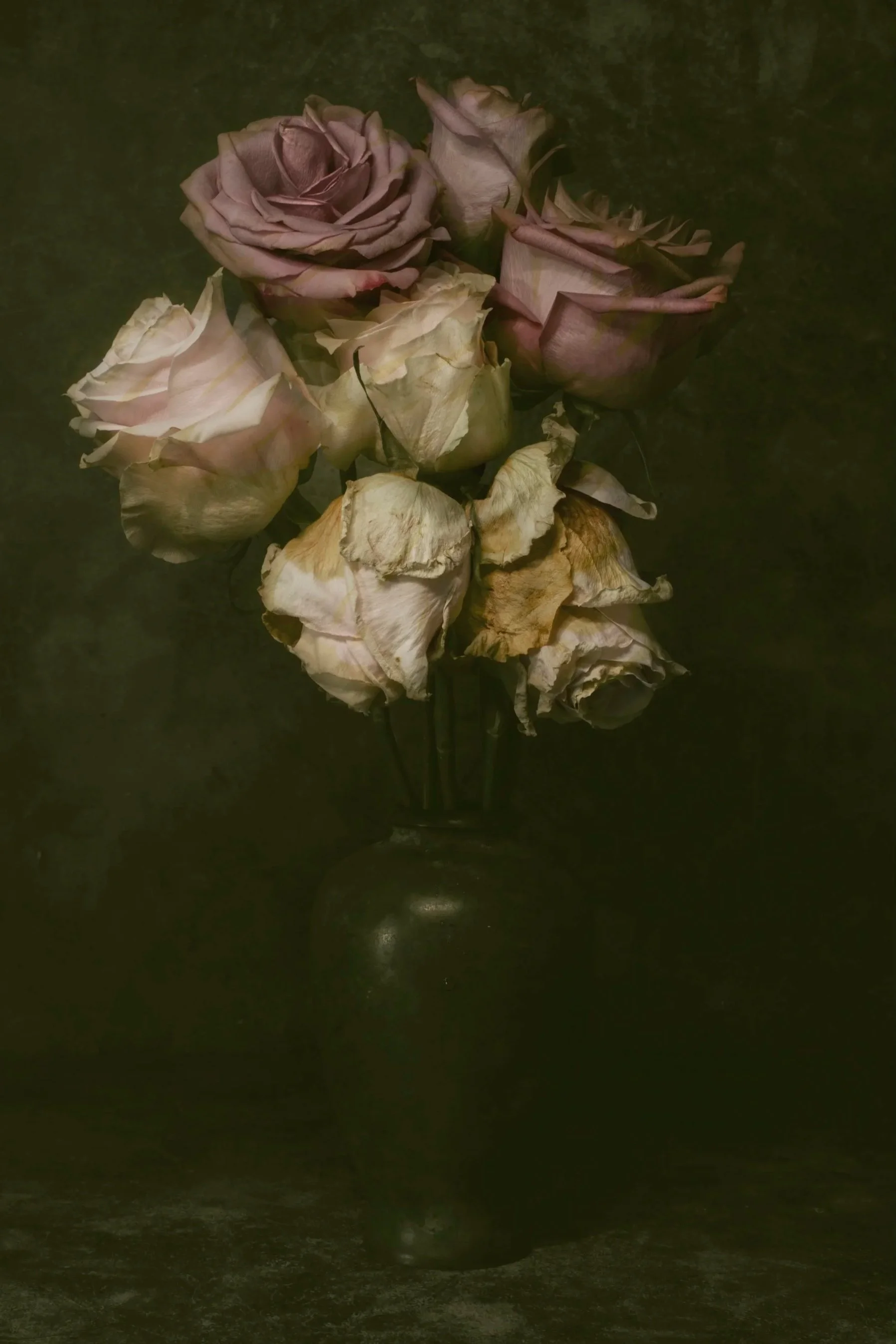 A bouquet of dried, faded roses in a dark vase against a black background. An image from the series 'Momento Mori' by the fine art photographer Will Arden.