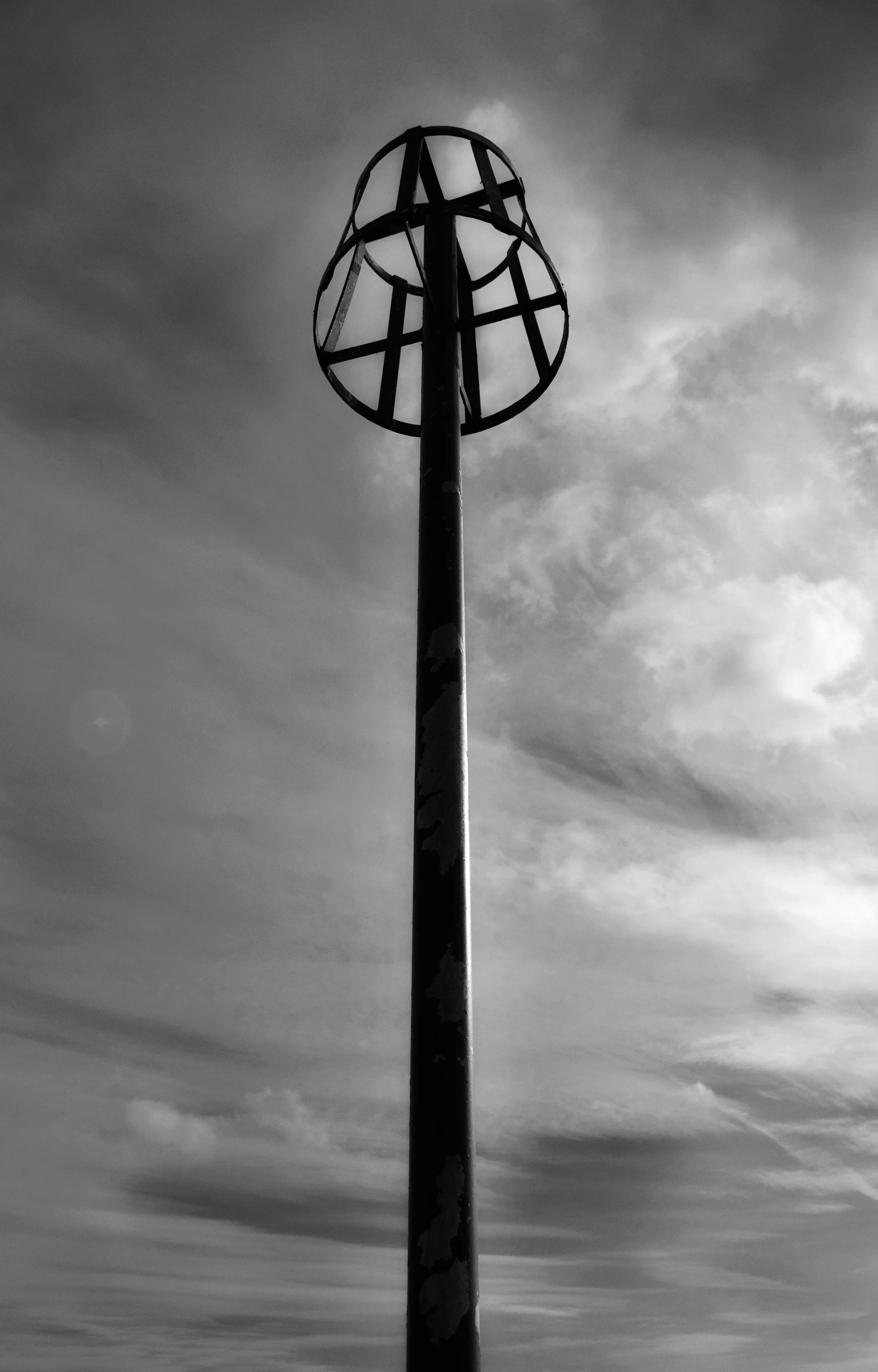 A tall, weathered metal pole with a spherical wireframe structure at the top, set against a cloudy sky.