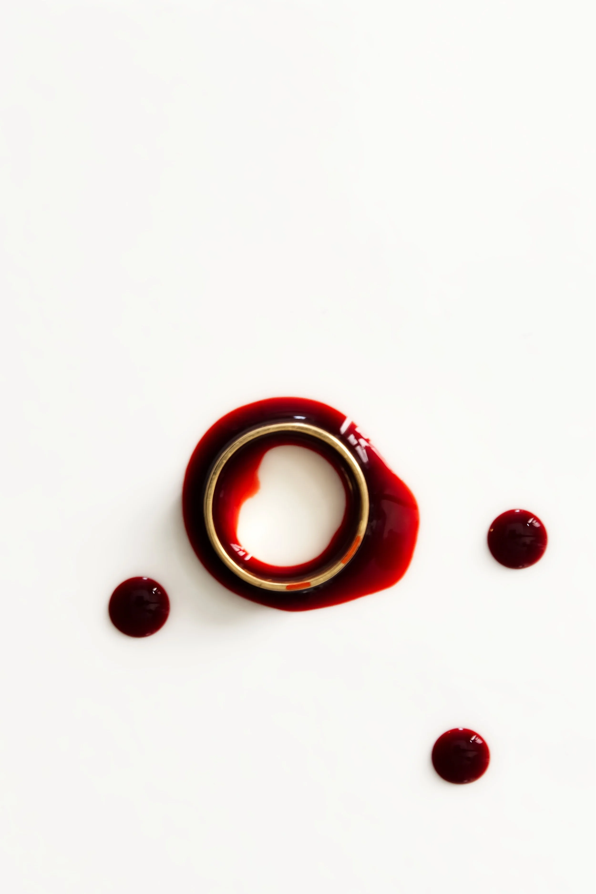 A bottle with red liquid and white cap, with red liquid spilled around it and three red drops around the bottle on a white surface.