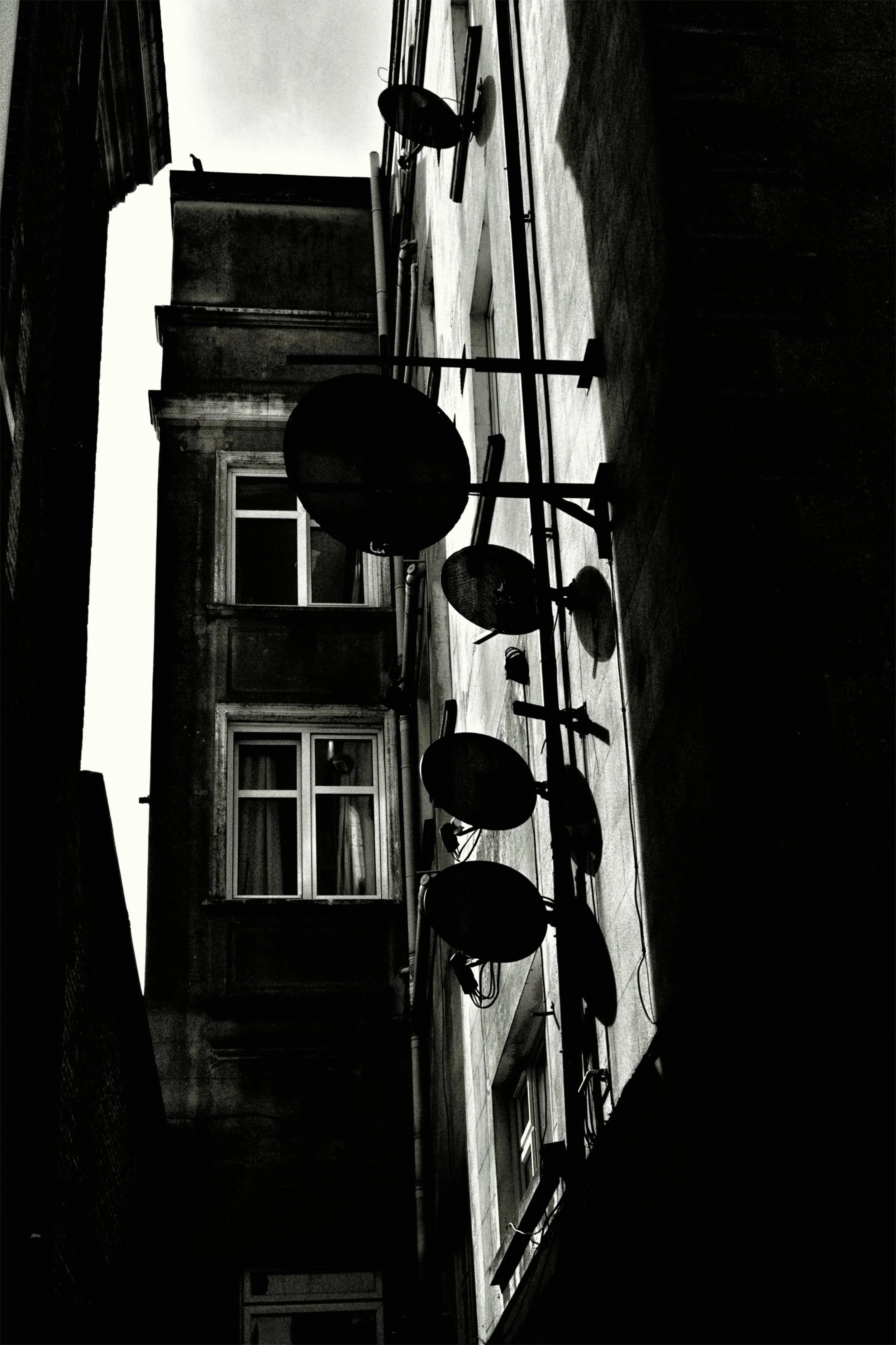 Black and white photo of an indoor gym or fitness studio with workout equipment, including exercise balls and mats, on a wooden floor near a window, with a brick wall background.