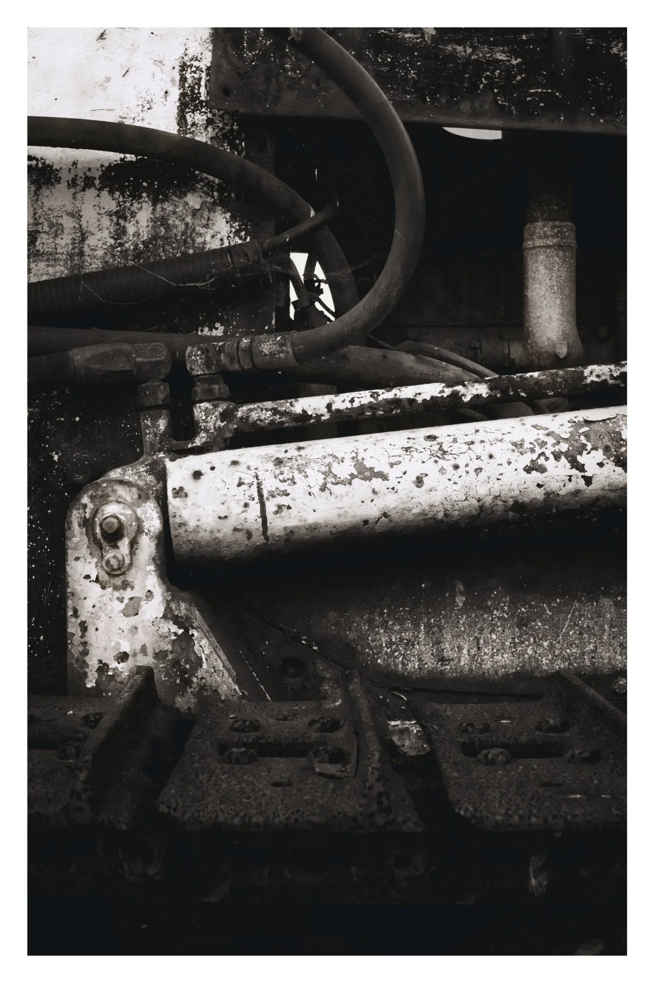 A close-up view of a dirty, worn, and weathered industrial machine part with pipes, bolts, and metal components covered in grime and rust.