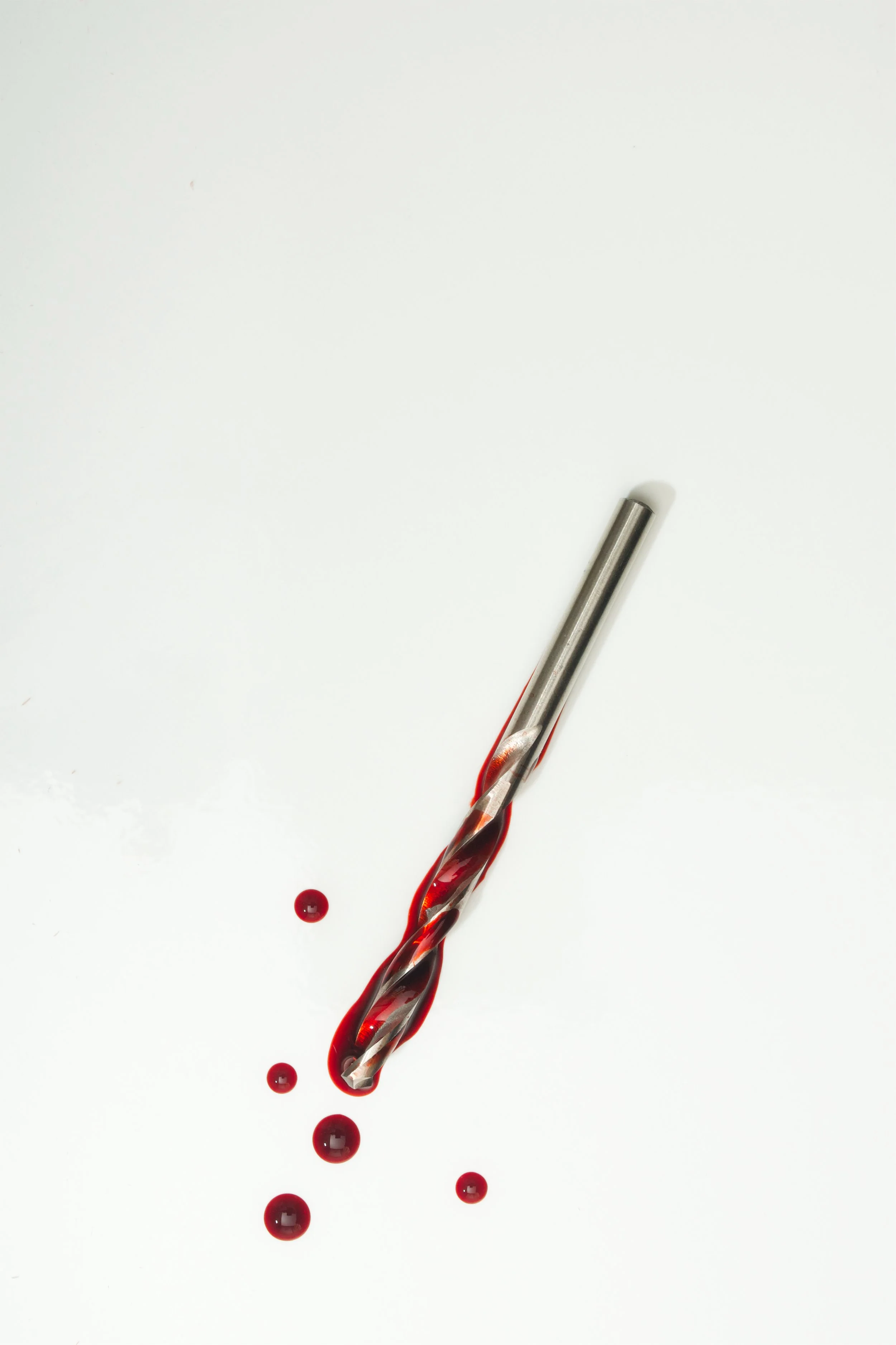 A test tube with red liquid spilling onto a white surface, creating small drops around it.