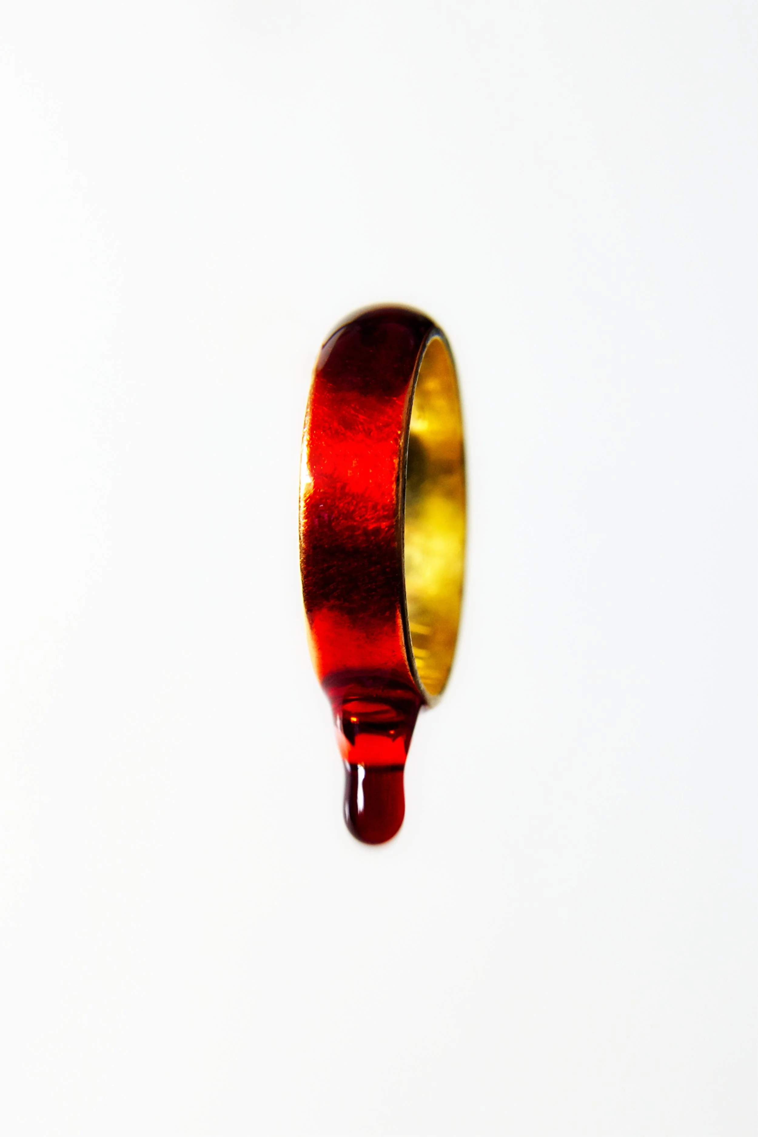 A gold ring with a red and black enamel top, with red liquid dripping from it against a white background.