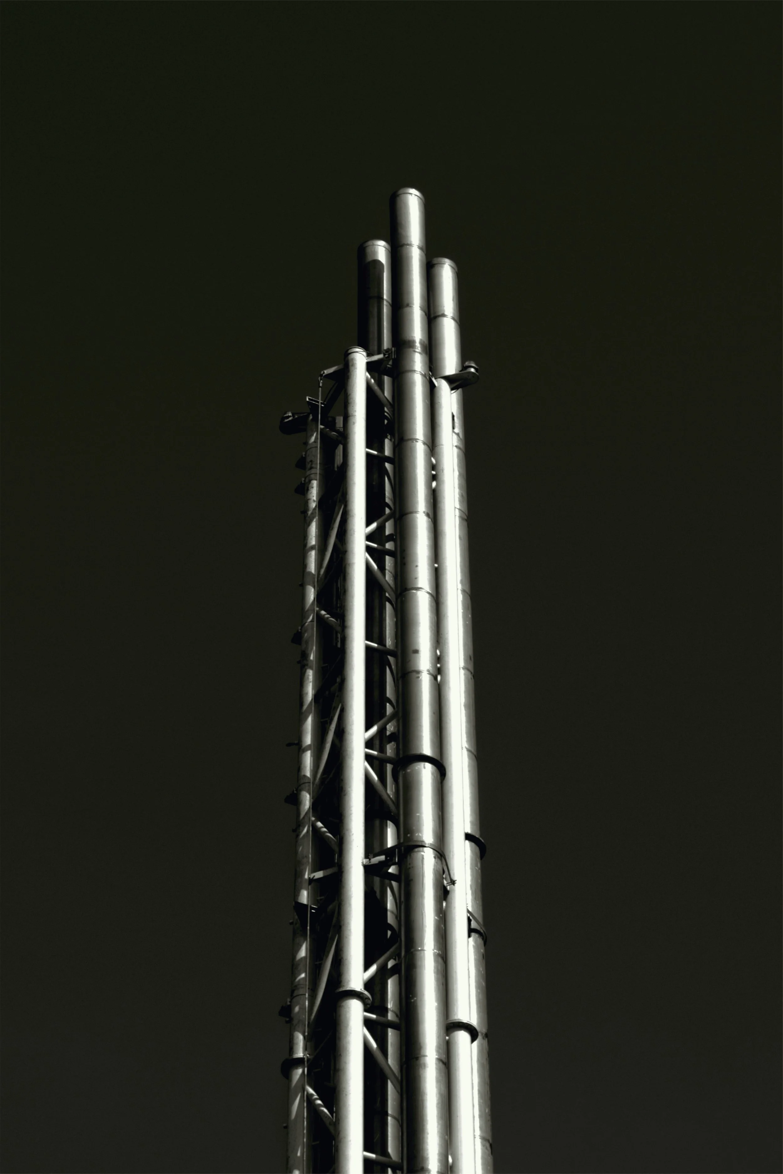 A tall industrial metal tower with multiple pipes against a dark, cloudy sky.