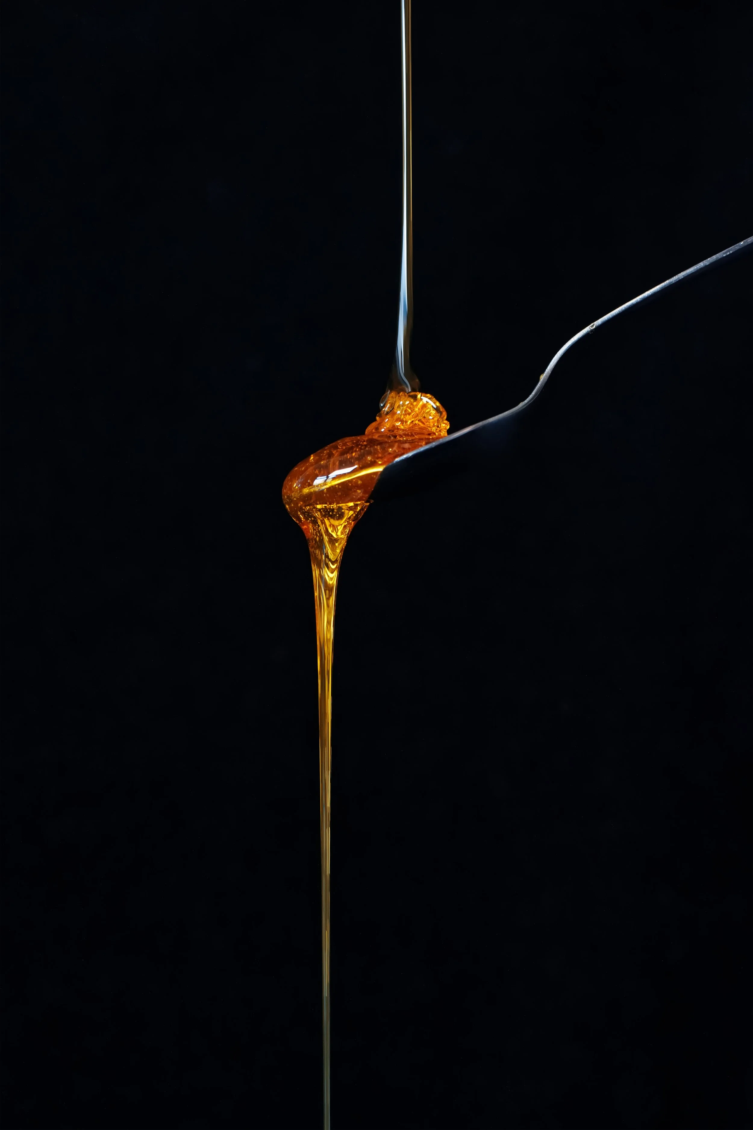 Close-up of honey or syrup dripping from a spoon against a black background.