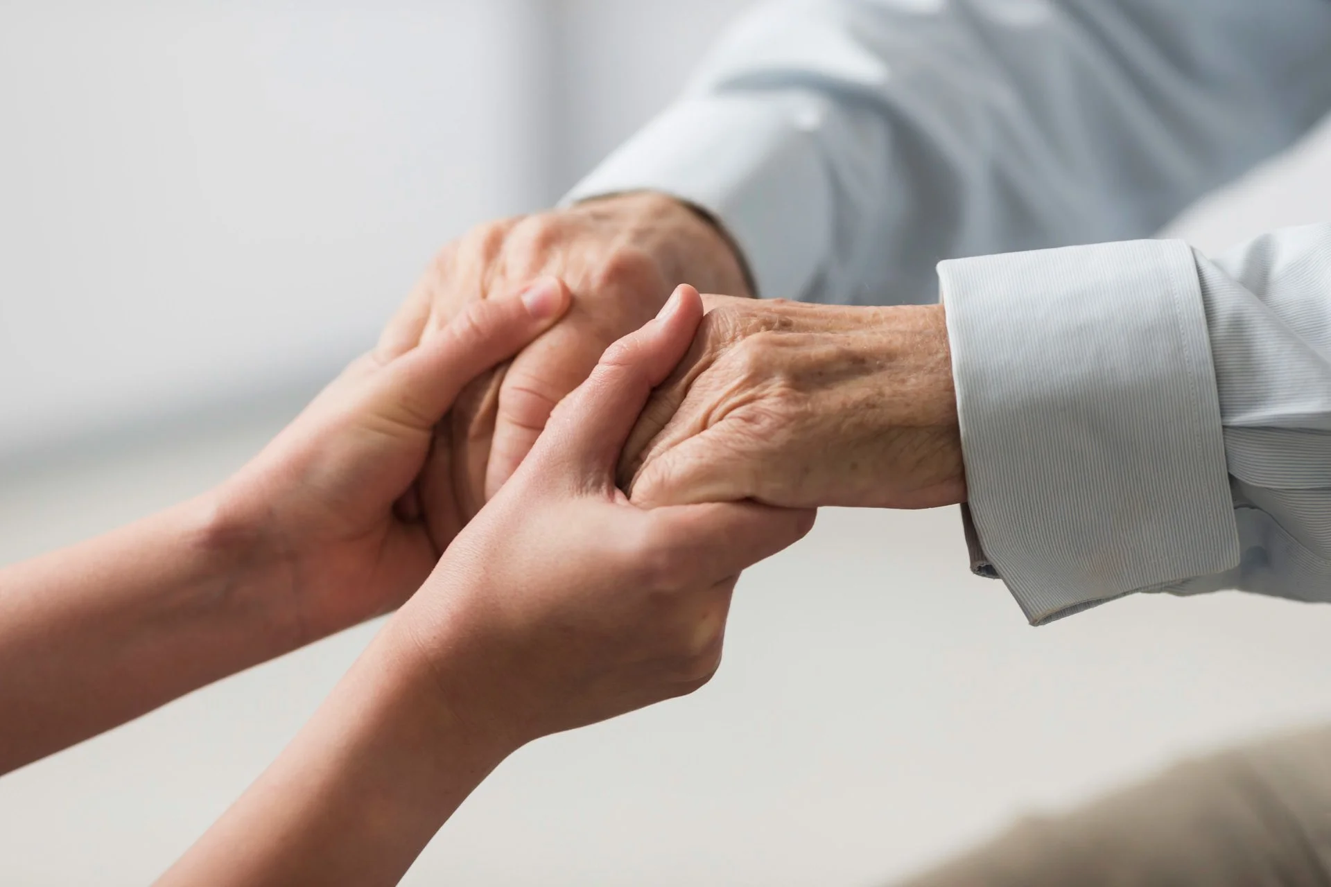 Two people holding hands, one of them elderly person in blue shirt