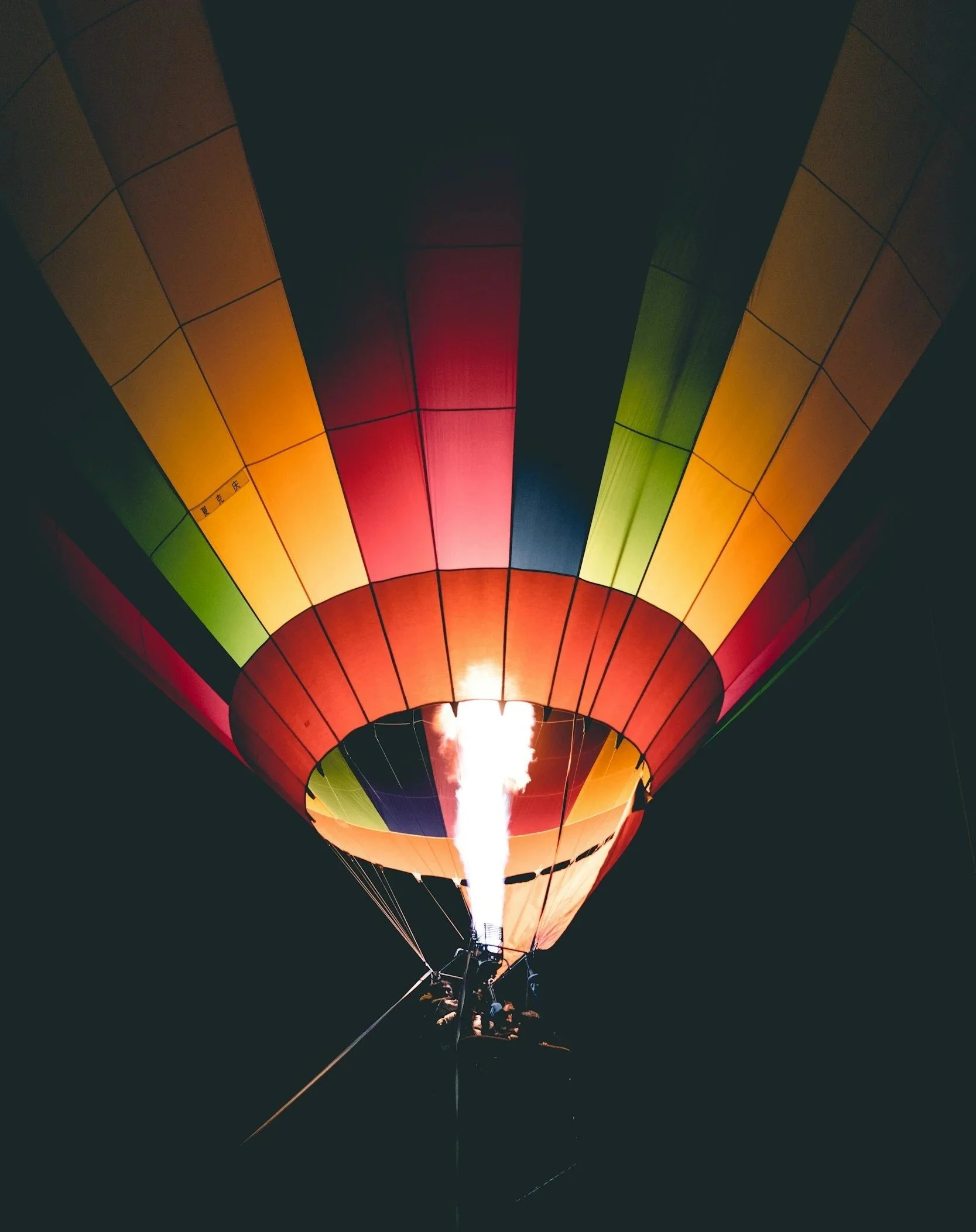 A multicoloured hot air balloon.  The picture has a black background, so the colours are vivid and the flame is visible.