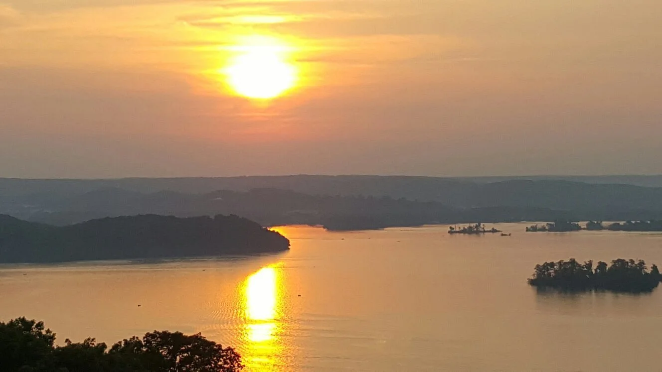 Sunset over a river with distant hills and small islands, reflecting golden light on the water.