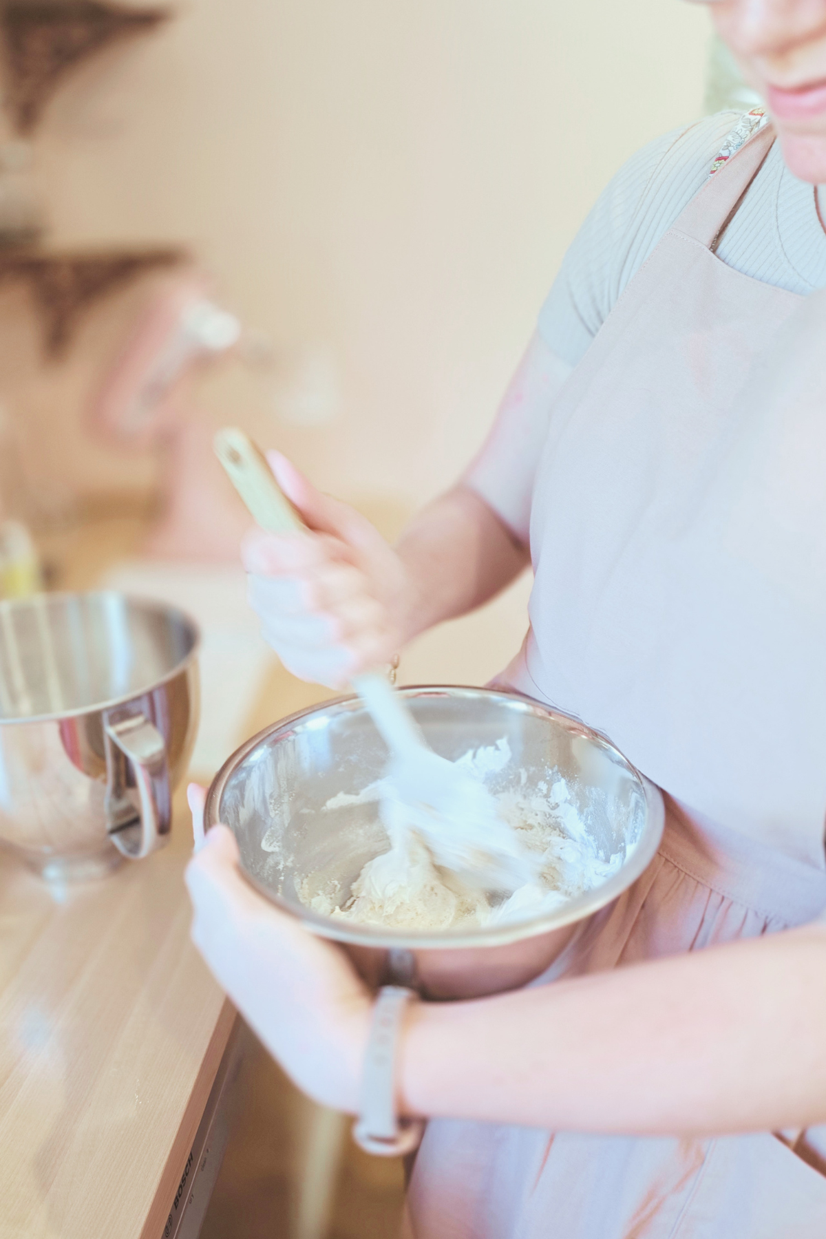 A person mixing ingredients in a metal bowl in a kitchen, with another person taking a picture of them.