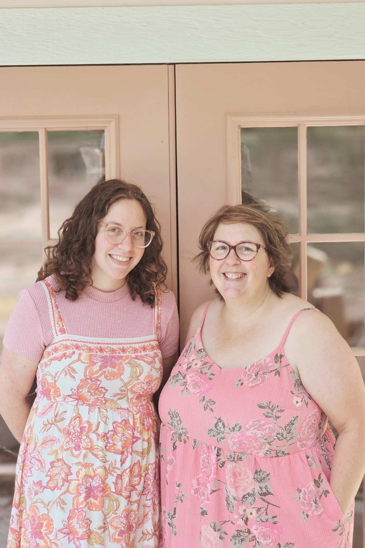 Two women standing in front of a wooden door with glass panels, smiling at the camera.