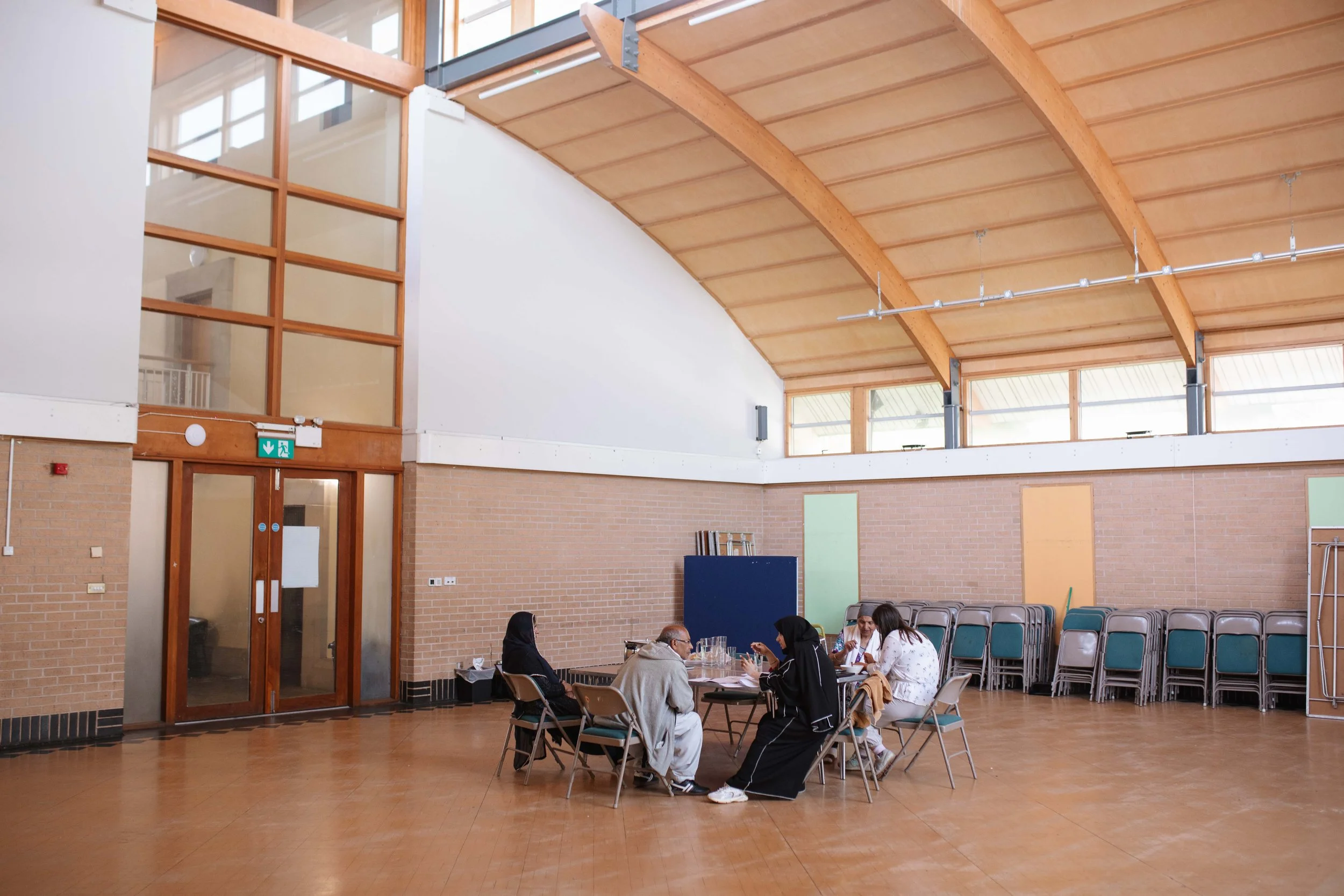 A group of people sitting at a long table inside a large room with brick walls and a wooden ceiling.
