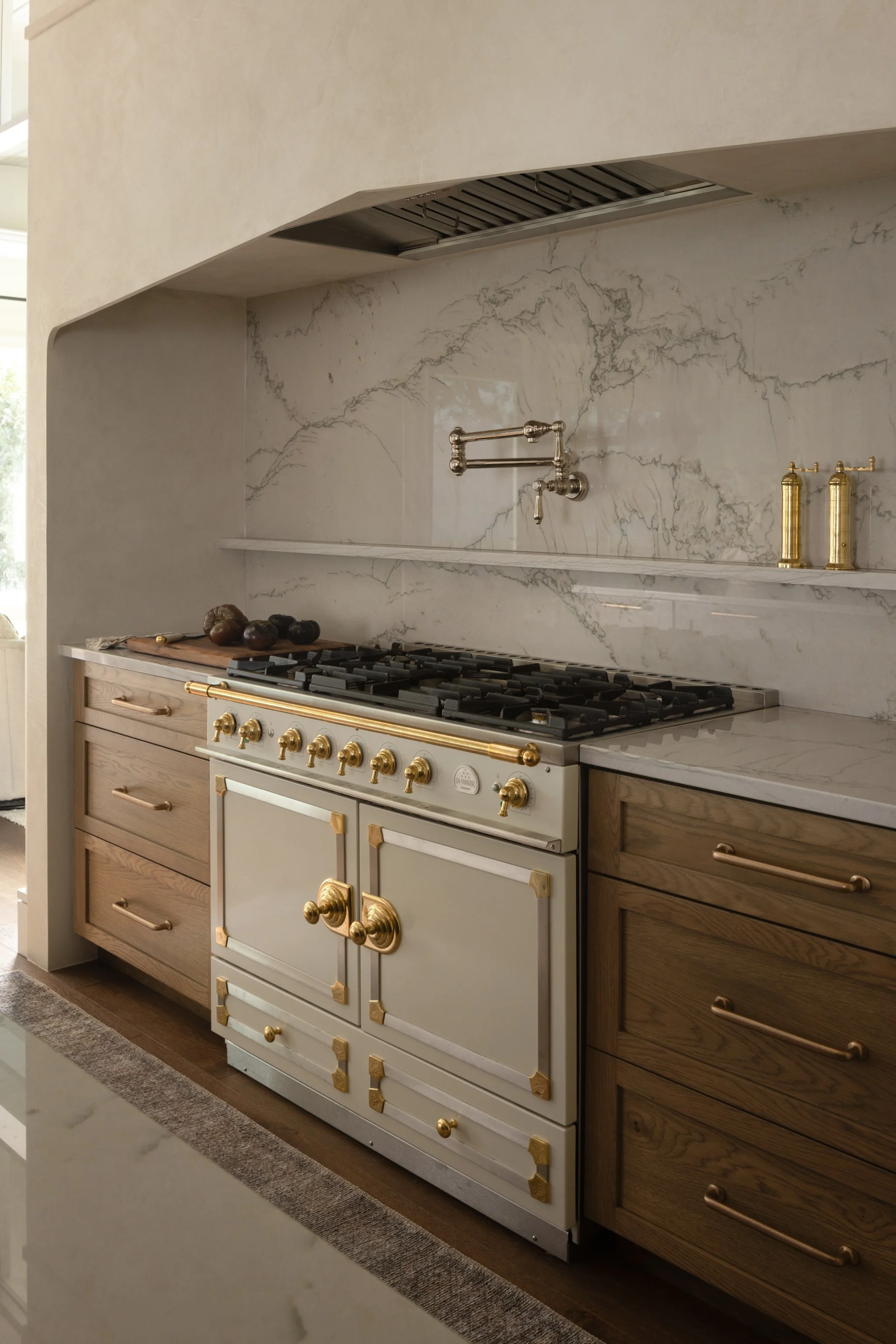 Kitchen with marble backsplash, vintage-style oven with gold accents, wooden cabinets, and a white marble countertop.