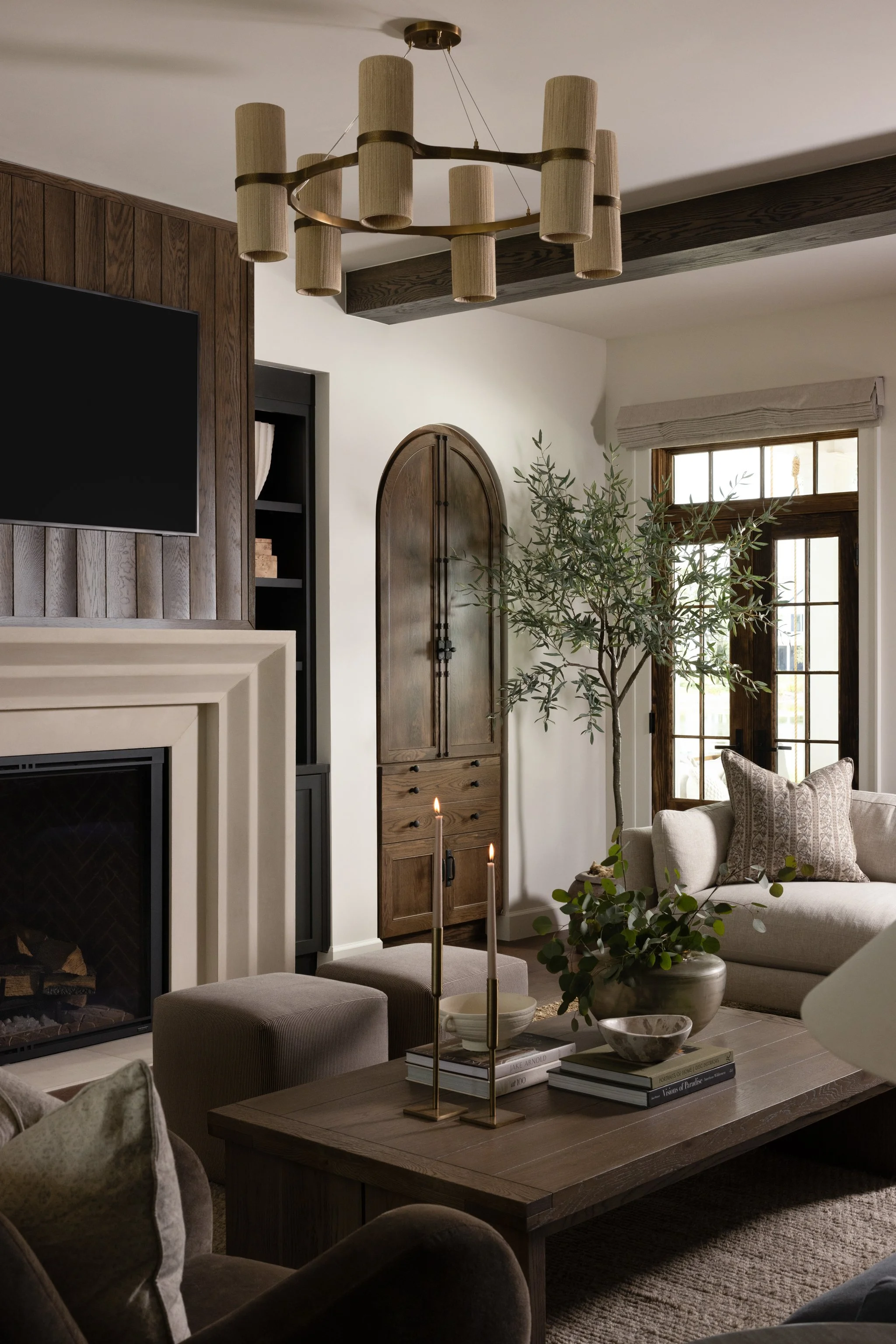 Living room with a fireplace, beige sofa, wooden coffee table, candles, potted plant, wooden cabinet, TV, and glass doors.