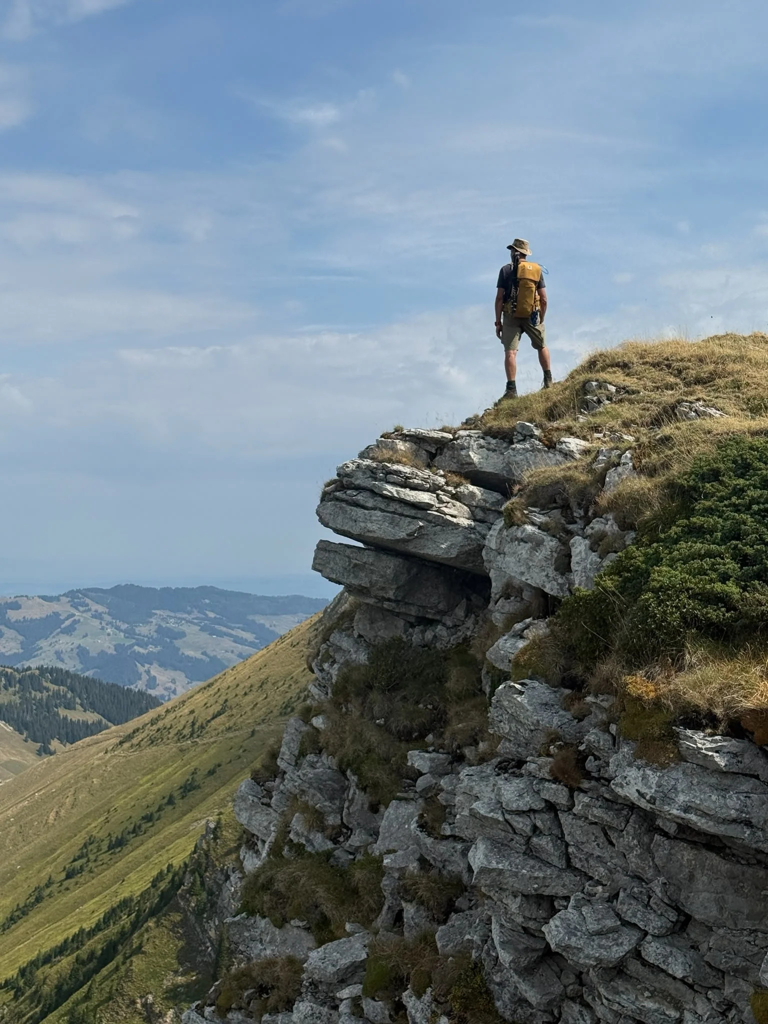Marc avec un sac à dos regarde la vallée depuis une falaise rocheuse en montagne. Photo: Laura Laning