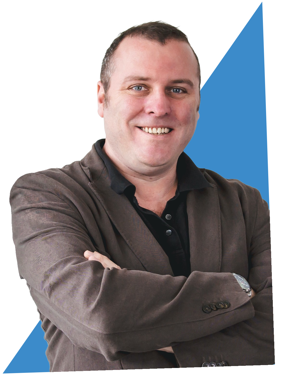A smiling man with crossed arms, wearing a brown blazer over a black shirt, with a blue geometric shape in the background.