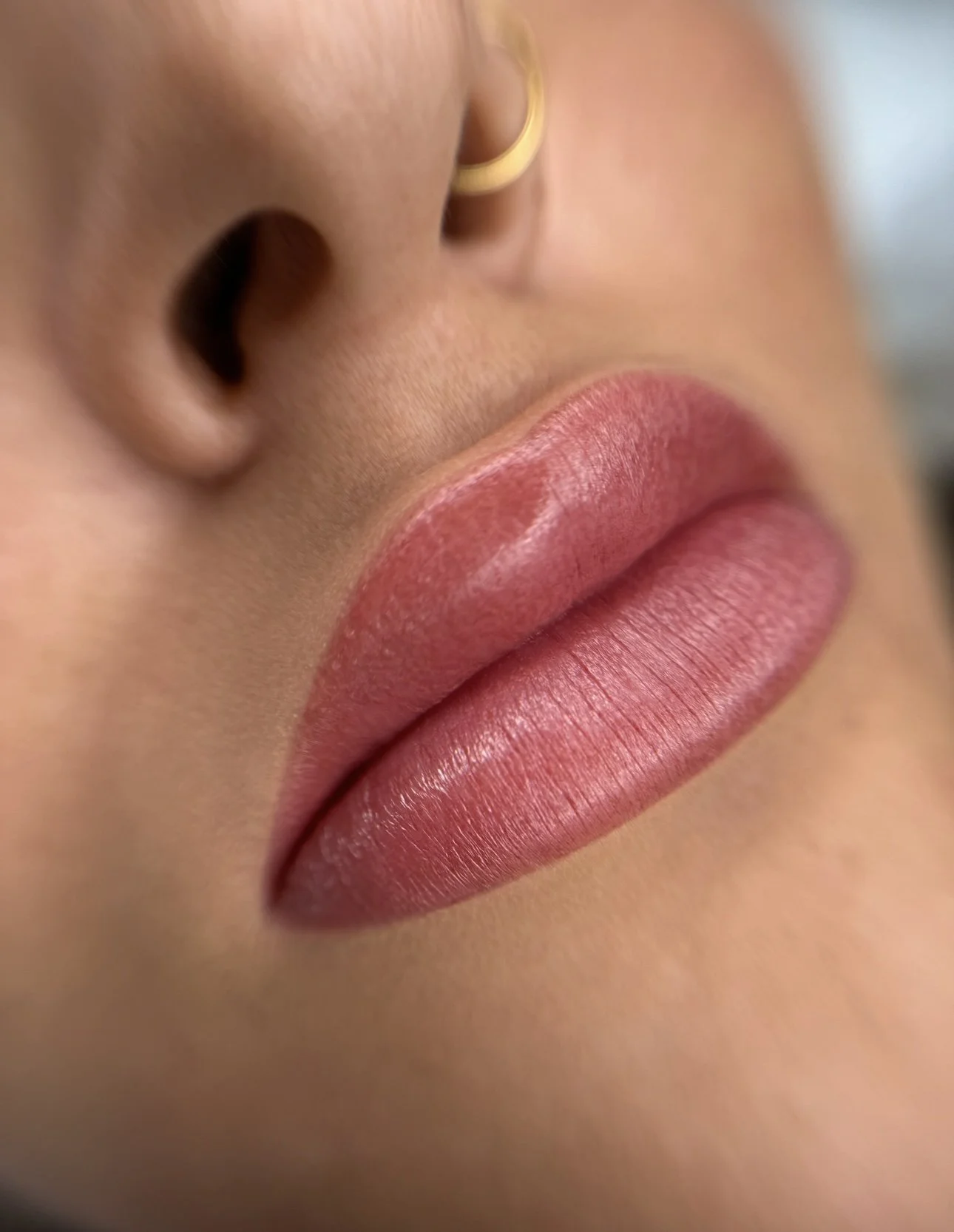 Nahaufnahme von Lippen mit pinkem Lippenstift, Nase mit Nasenpiercing, Teil eines Goldrings im Ohr.