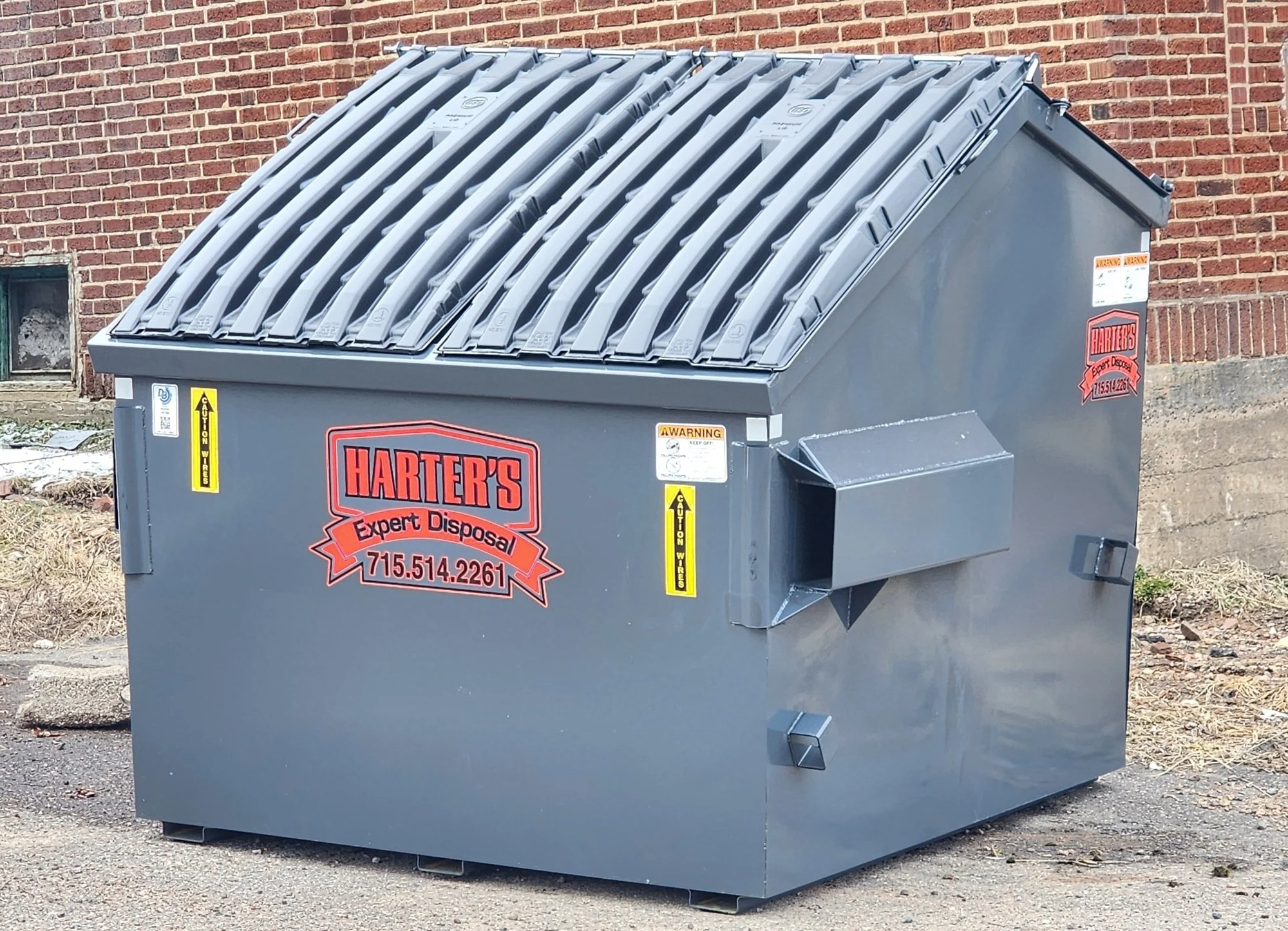 Gray commercial dumpster with company logo and contact information, placed outdoors near a brick wall.