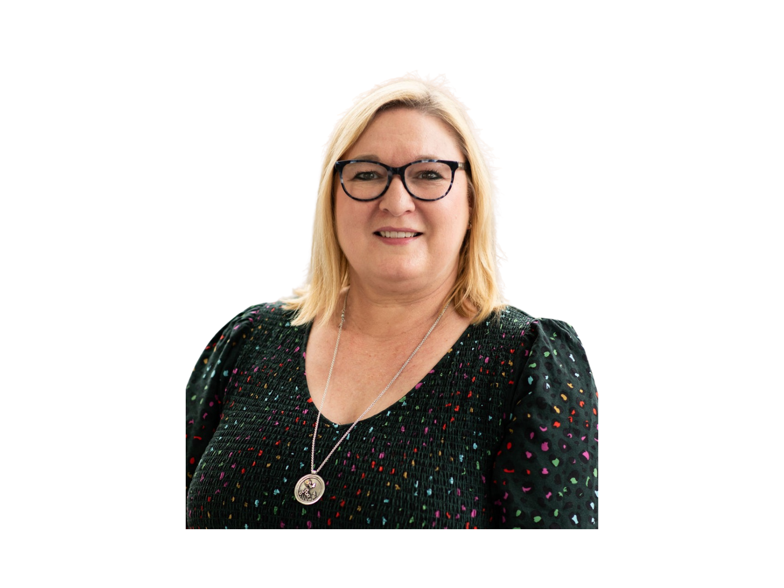 A woman with blonde hair and glasses, wearing a black, colorful, patterned top and a silver necklace with a large circular pendant.