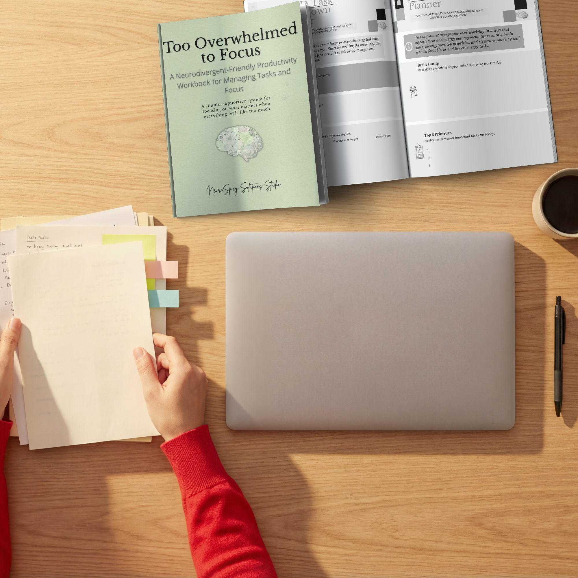 Open notebook with handwritten notes, sticky tabs on left edge, and partially visible printed documents on a light wooden desk. A person's hand is turning a page in the notebook, and there is a pen on the right side. A sheet of paper and a cup of coffee are also visible.