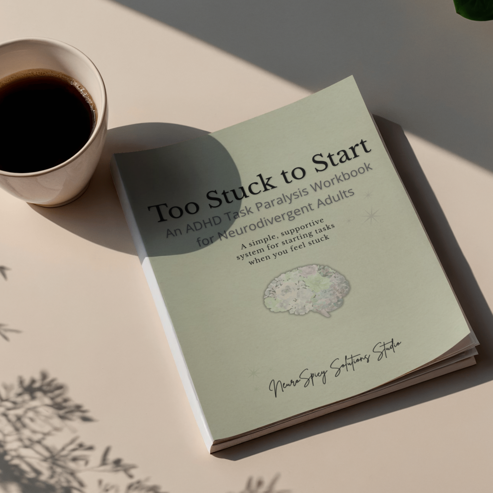 A white mug filled with black coffee placed on a flat white surface. Part of a book titled 'Stuck to Start' with subtitle and other text is visible, along with some shadow from an out-of-frame plant.