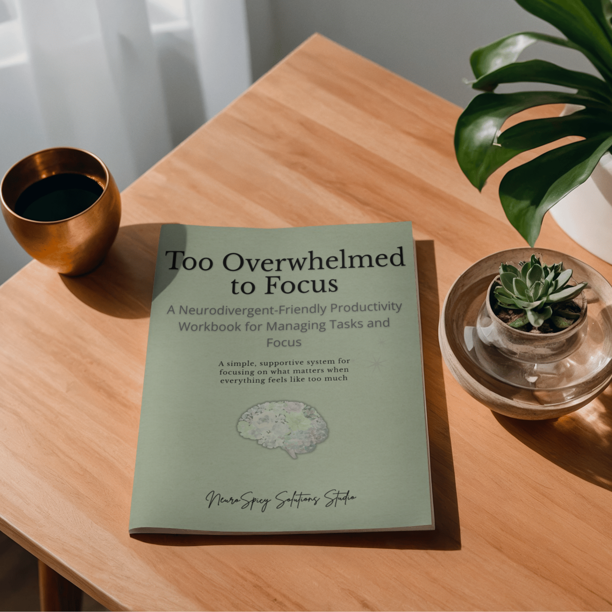 A wooden table with a copper cup filled with coffee, a green booklet titled 'Too Overwhelmed to Focus,' a small potted succulent plant, and part of a large green leaf in the top right corner.