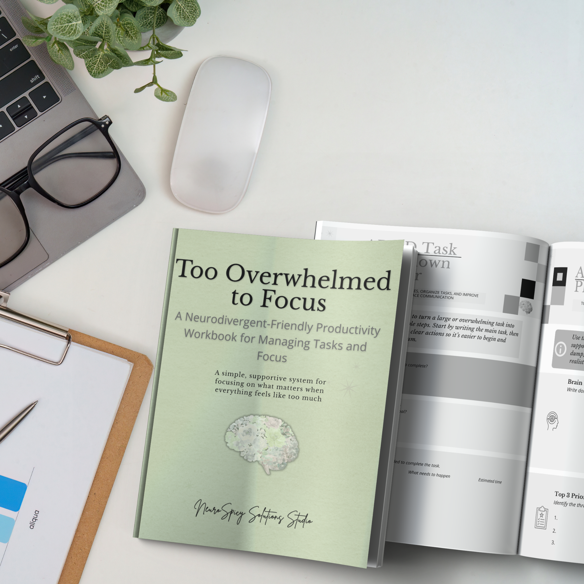 A workspace with a laptop, a pair of black glasses, a green plant, a white wireless mouse, documents, a pen, and a booklet titled 'Too Overwhelmed to Focus'.