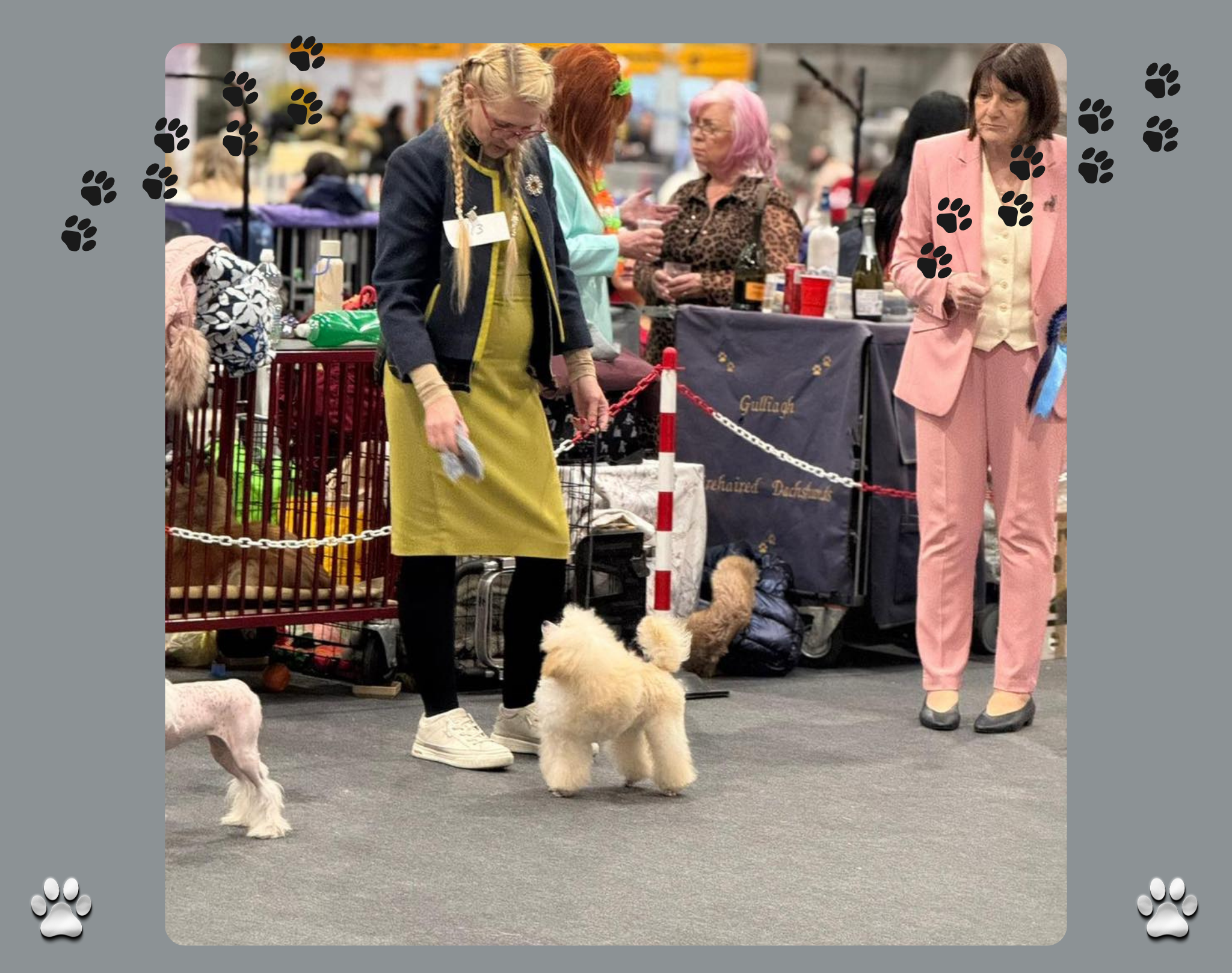 People at a dog show, with one woman in a yellow and black outfit and a dog, and others in colourful attire, in Crufts indoor exhibition space.