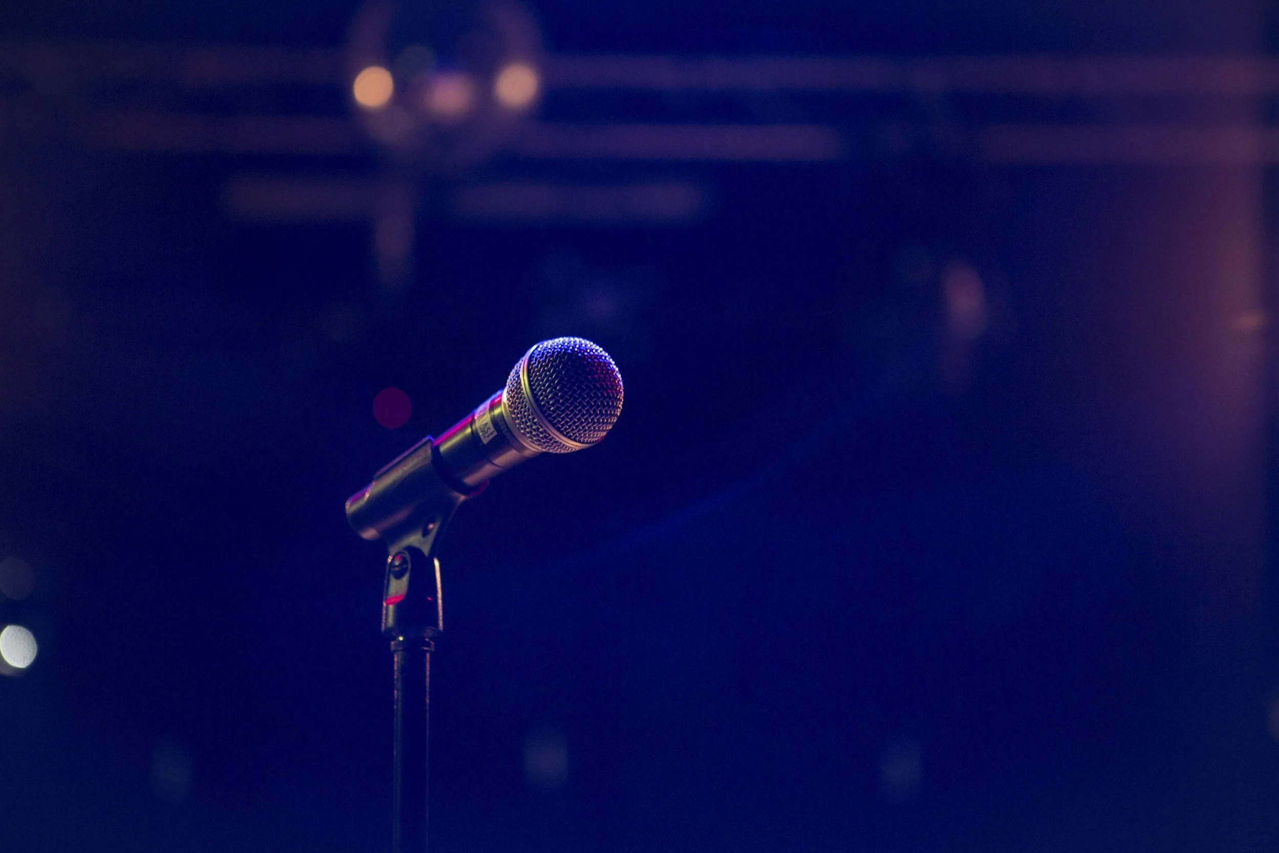 A microphone on a stand with a dark, blurred background featuring purple and blue lighting.