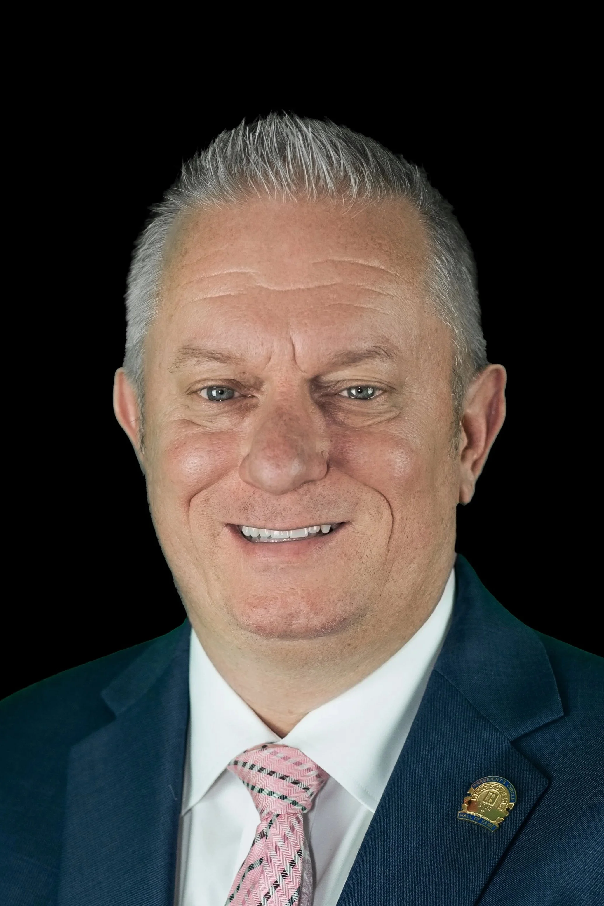 Jason Jakus headshot photo in a blue suit and pink tie. 