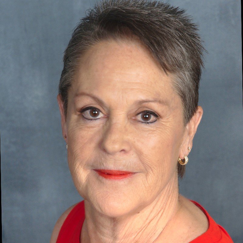 Close-up portrait of a mature woman with short, dark gray hair, wearing red lipstick, small gold earrings, and a red top against a gray background.