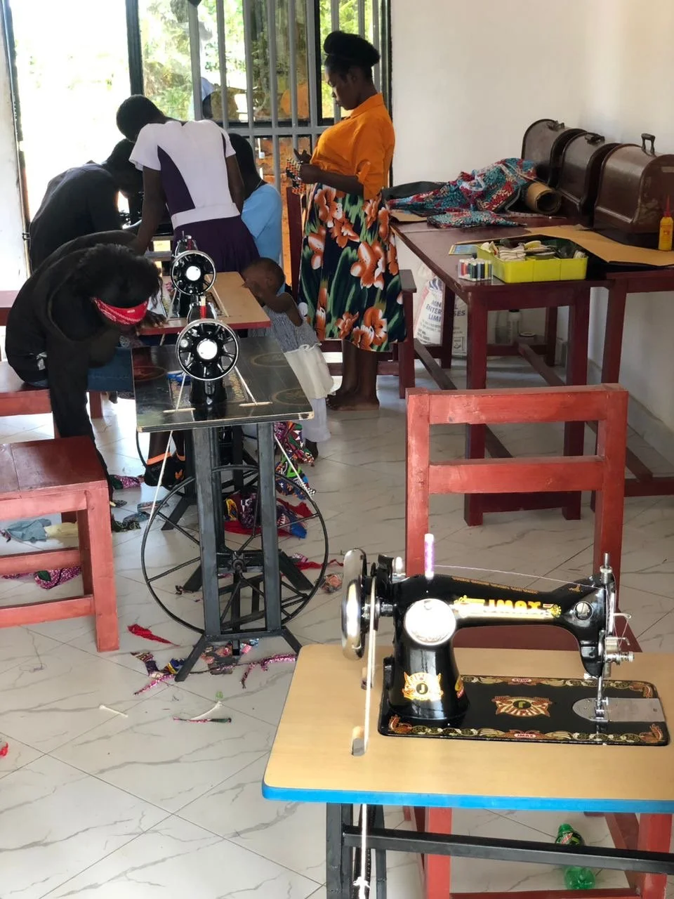 People working on sewing projects in a room with sewing machines, fabric, and thread.
