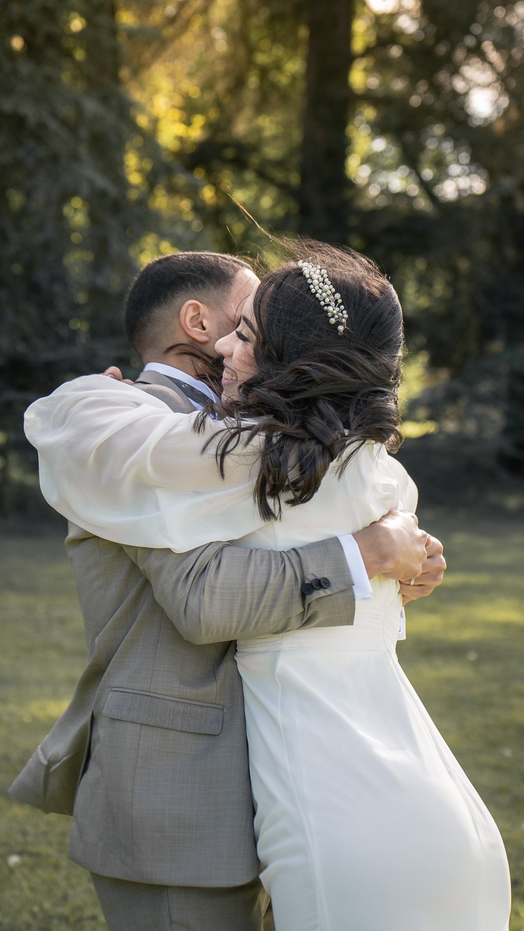 Un couple en costume de mariage s'embrasse tendrement dans un environnement extérieur verdoyant.