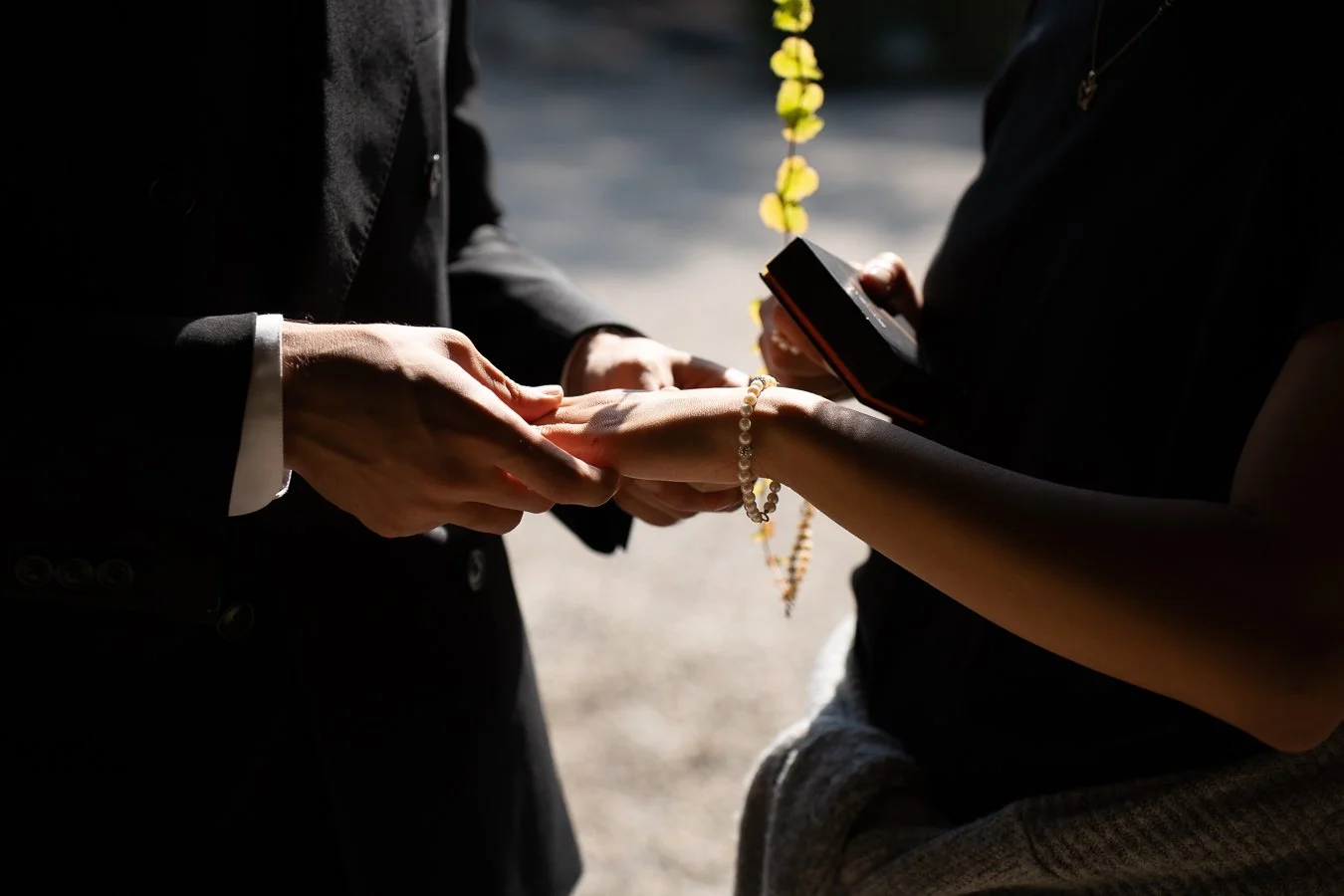 Un couple échange un anneau lors d'une cérémonie de mariage, avec une personne tenant un livre ou un dispositif pour lire, en plein air.