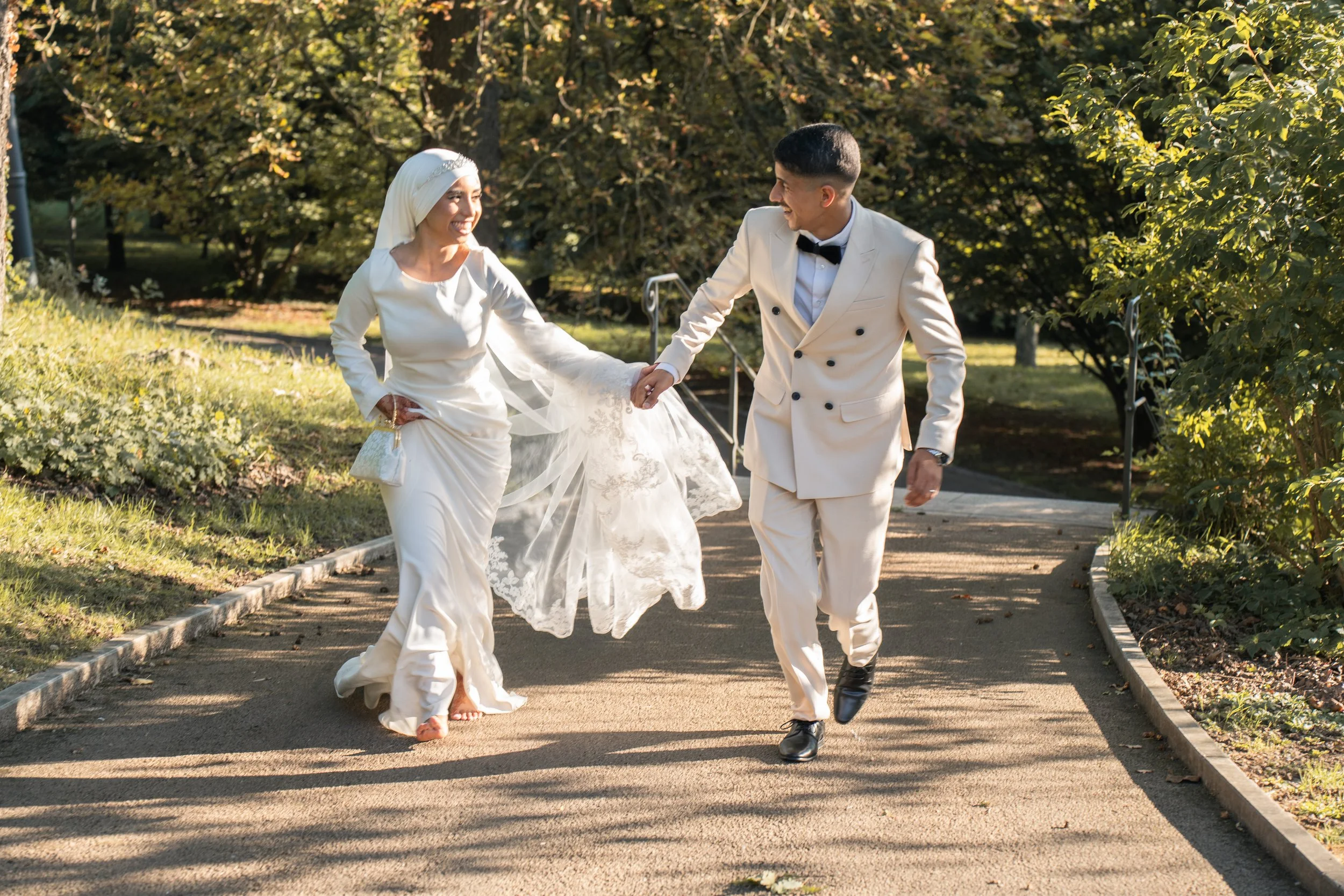 Un couple habillé pour un mariage, marchant dans un parc en automne, tenant la main, souriant et heureux.