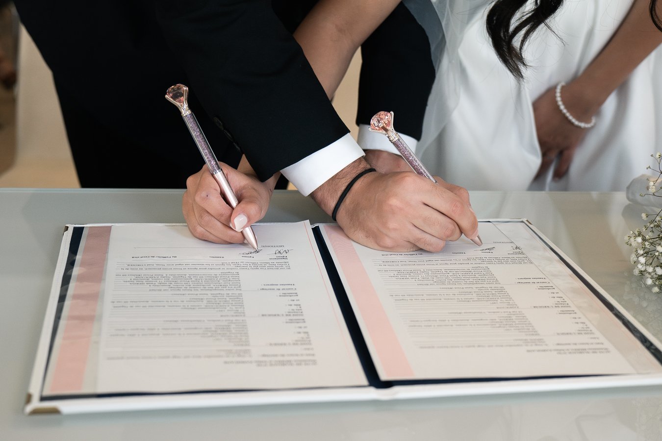 Deux personnes en costume signent un document officiel sur une table. L'aperçu montre des mains tenant des stylos aux styles décoratifs.