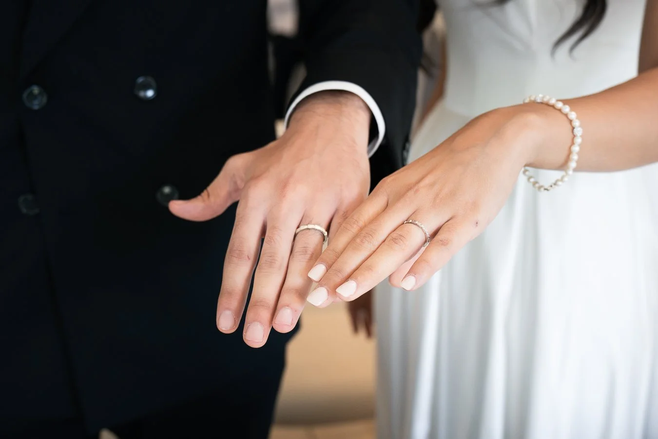 Mains de mariés portant des alliances, main de l'homme en costume noir et main de la femme en robe blanche avec bracelet de perles.